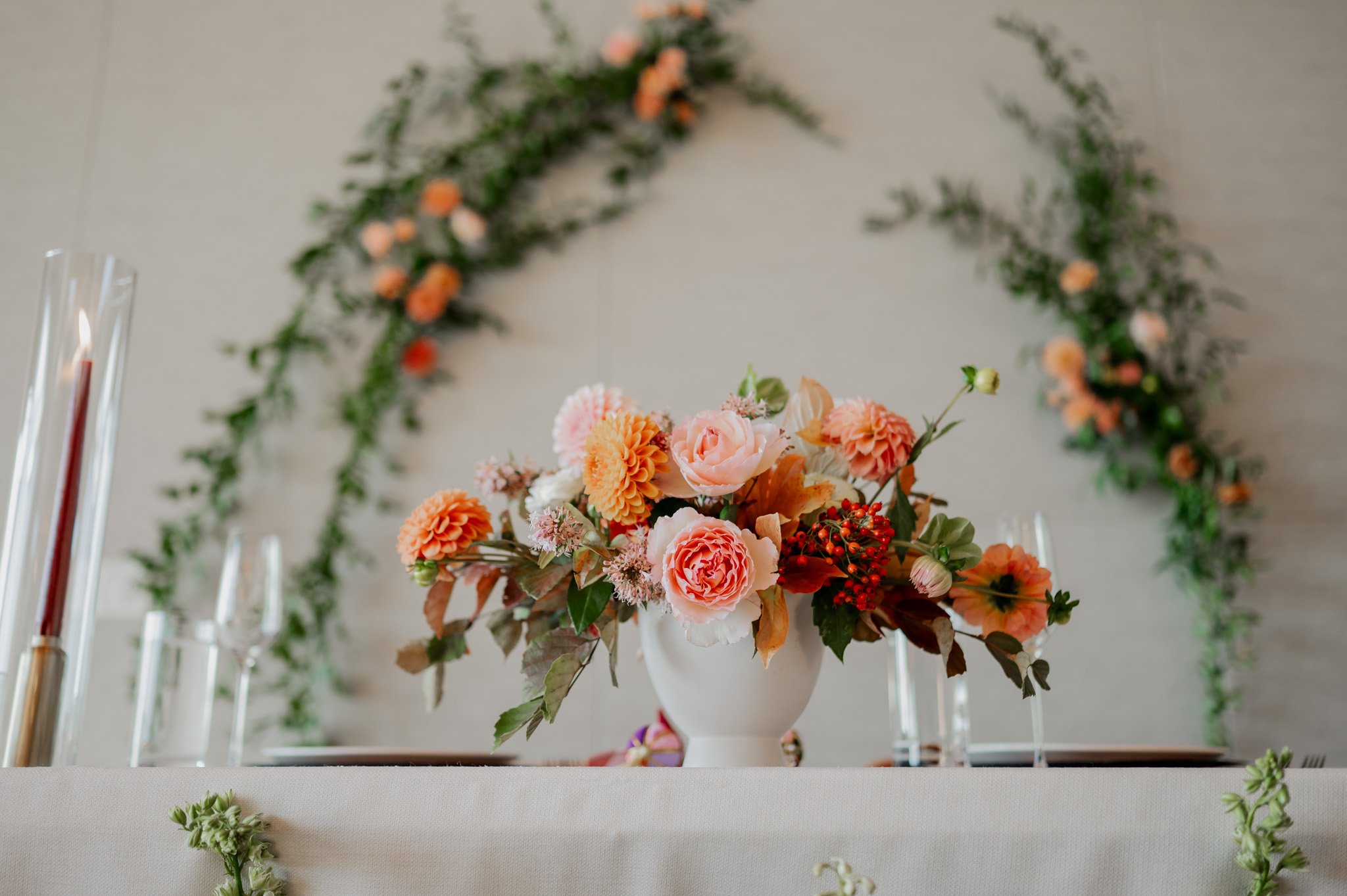 A floral centerpiece with pink and orange flowers, surrounded by lush greenery, graces the table at an Amaterra Winery wedding, with candles glowing softly in the background.