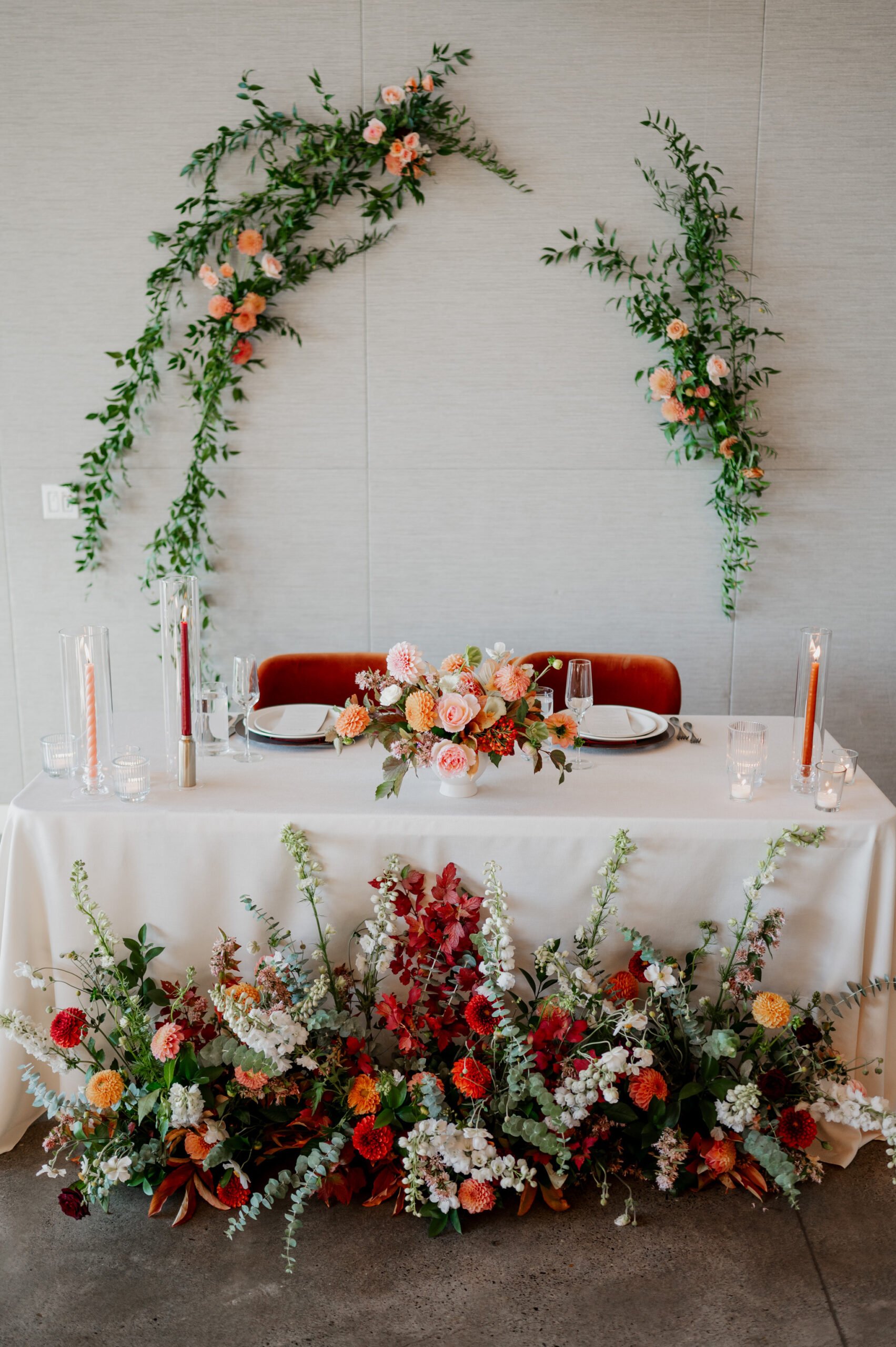 Elegant wedding table set against a gray wall backdrop at Amaterra Winery, featuring lush floral arrangements and greenery. Blush-colored flowers and soft candlelight create a romantic ambiance perfect for capturing unforgettable wedding photos.