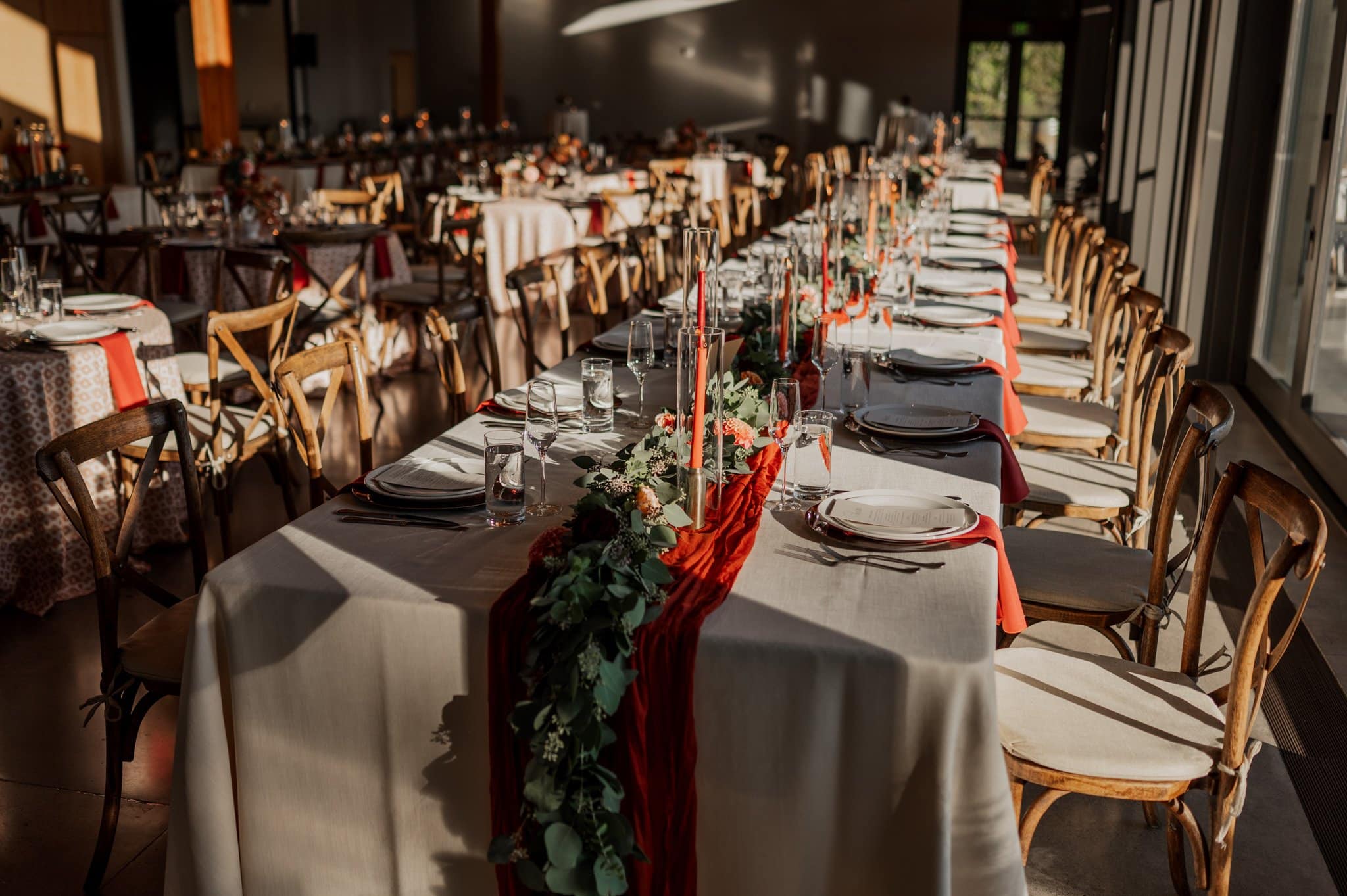 Elegant dining table setup with a red table runner, candles, and greenery, surrounded by wooden chairs in a sunlit room—perfect for capturing stunning Amaterra Winery wedding photos.