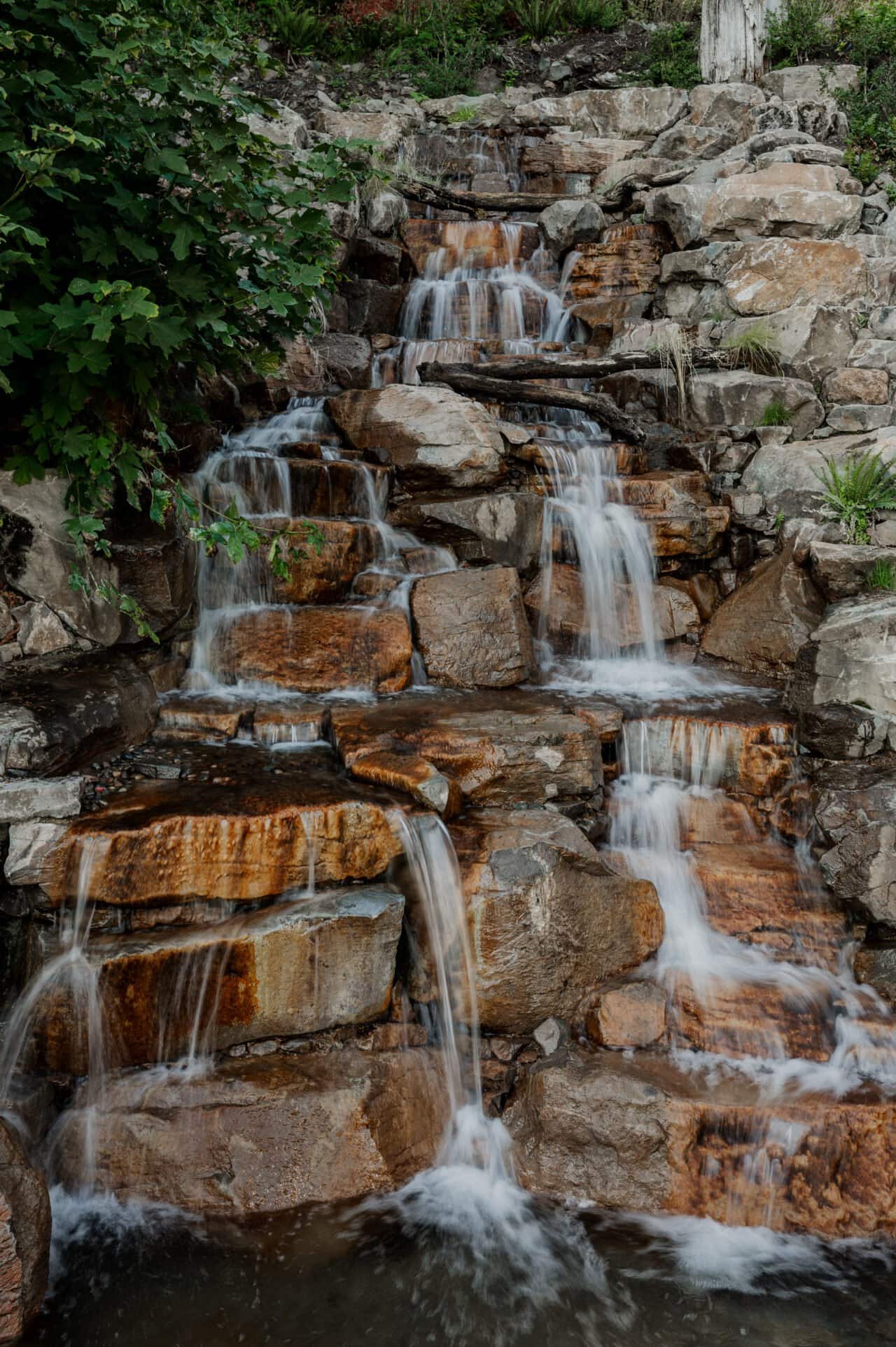 A small waterfall cascades over layered rocks surrounded by greenery, providing the perfect backdrop for enchanting Amaterra Winery wedding photos.