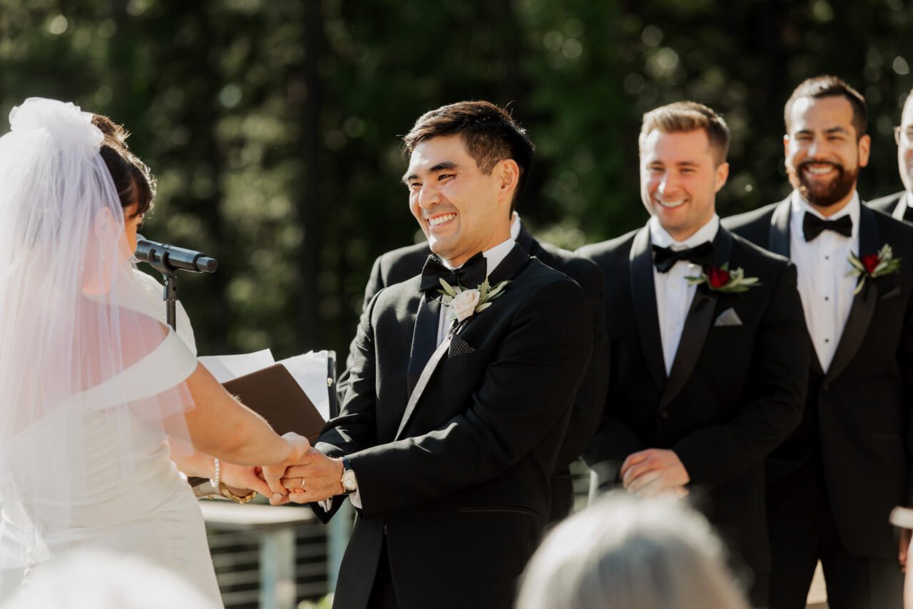 A groom and bride exchange vows outdoors at Amaterra Winery, surrounded by smiling groomsmen in formal attire, capturing the perfect wedding photos.