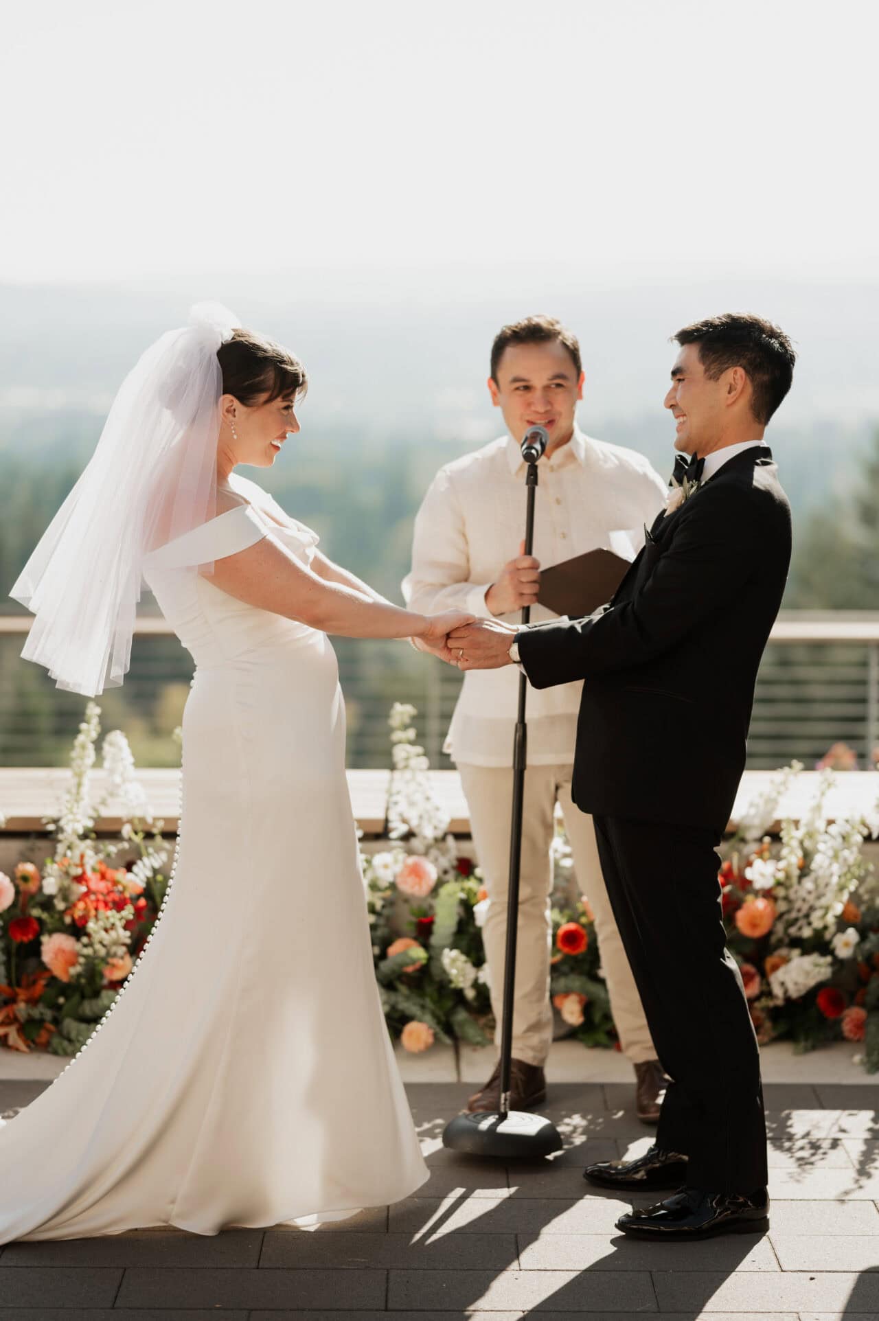 A couple exchanges vows outdoors at Amaterra Winery, holding hands with an officiant nearby. Floral arrangements decorate the background, capturing the essence of a perfect wedding photo.