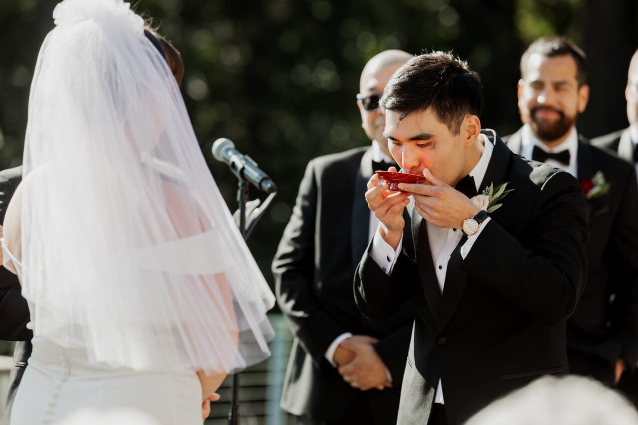 During an Amaterra Winery wedding, the groom savors a slice of watermelon in his suit, while the bride and groomsmen create a picturesque backdrop.