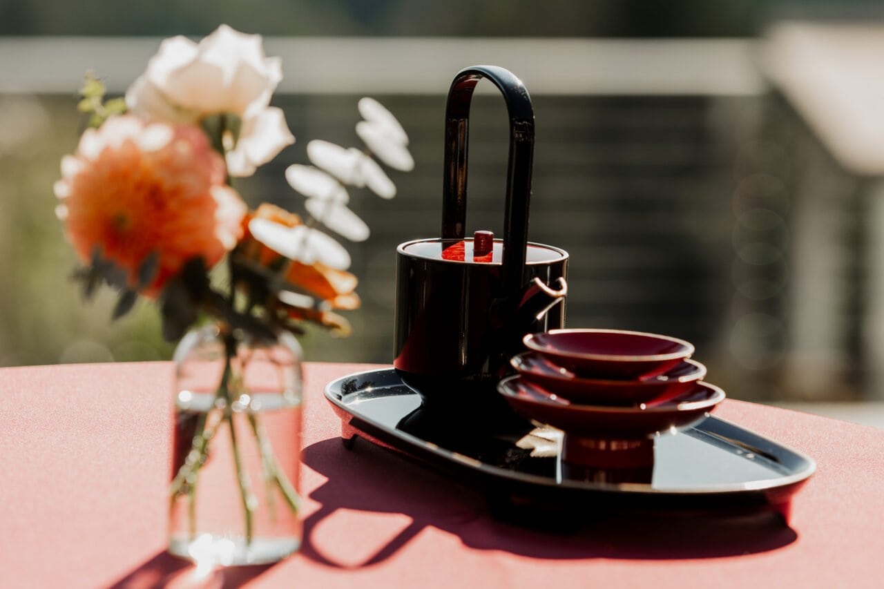 A red and black tea set with stacked cups on a tray graces the table, echoing the elegance of Amaterra Winery wedding photos, while a vase of flowers adds a touch of romance.