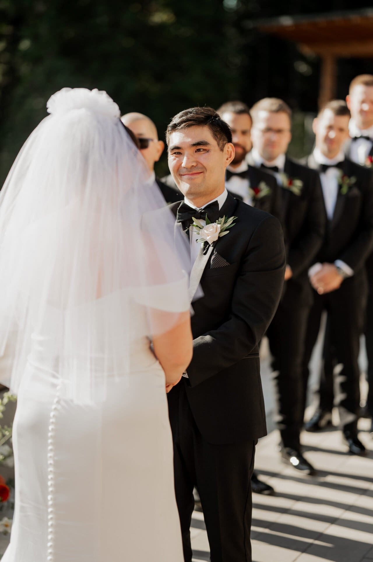 A bride and groom hold hands during their picturesque outdoor ceremony at Amaterra Winery, surrounded by groomsmen in suits.