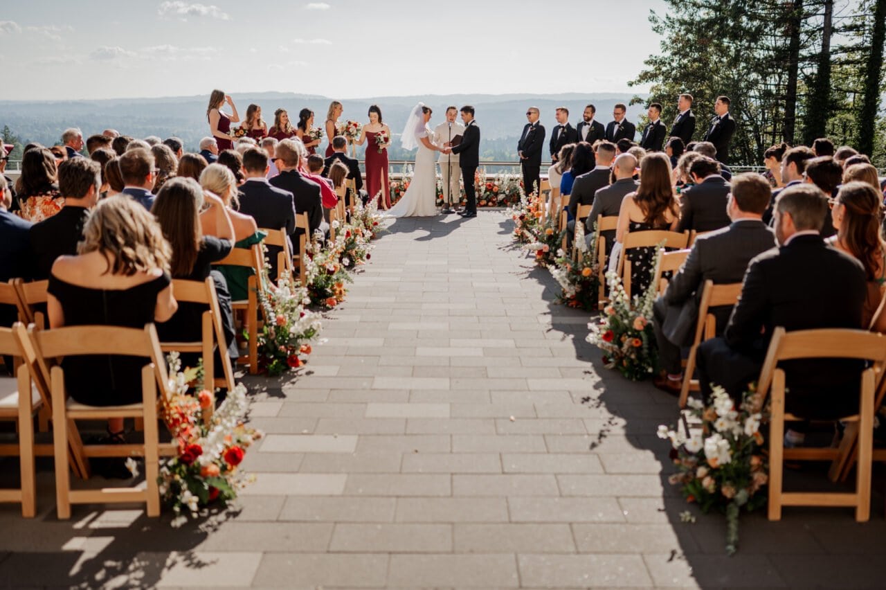 Amid the breathtaking scenery of Amaterra Winery, the bride and groom stand at the altar surrounded by loved ones. Guests are seated on either side, creating a perfect setting for unforgettable wedding photos that capture every magical moment.