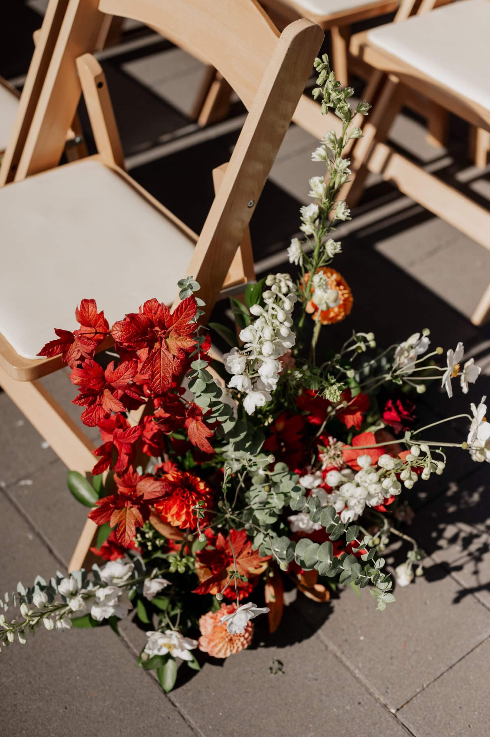 A wooden chair, adorned with a vibrant bouquet of red, white, and orange flowers, graces the sunny stone pathway—a scene reminiscent of enchanting Amaterra Winery wedding photos.