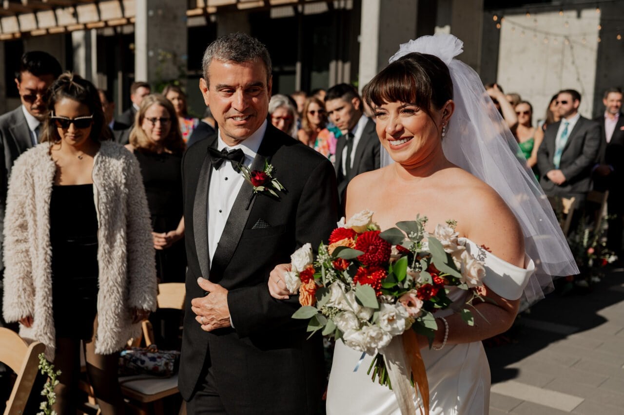A bride and a man walk down the aisle at an outdoor wedding, surrounded by guests, their moment beautifully captured in Amaterra Winery wedding photos.