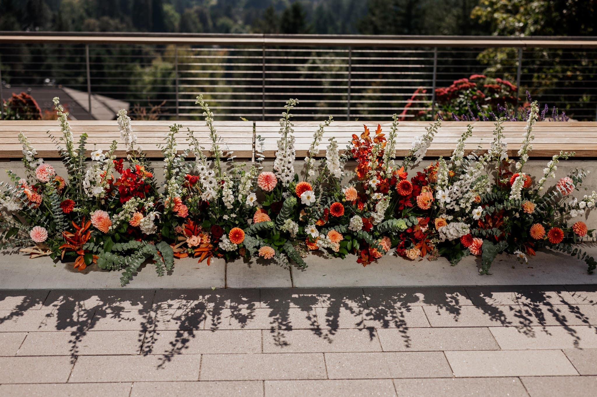 A vibrant flower arrangement of red, orange, and white blooms gracefully lines a railing in a sunlit outdoor setting—perfect for capturing stunning Amaterra Winery wedding photos.