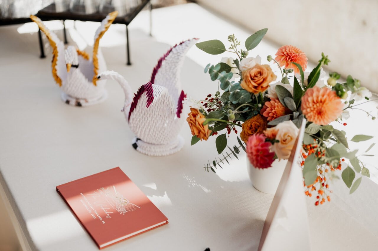 A table adorned with origami cranes, a floral arrangement, and a red book awaits the capturing of Amaterra Winery wedding photos.