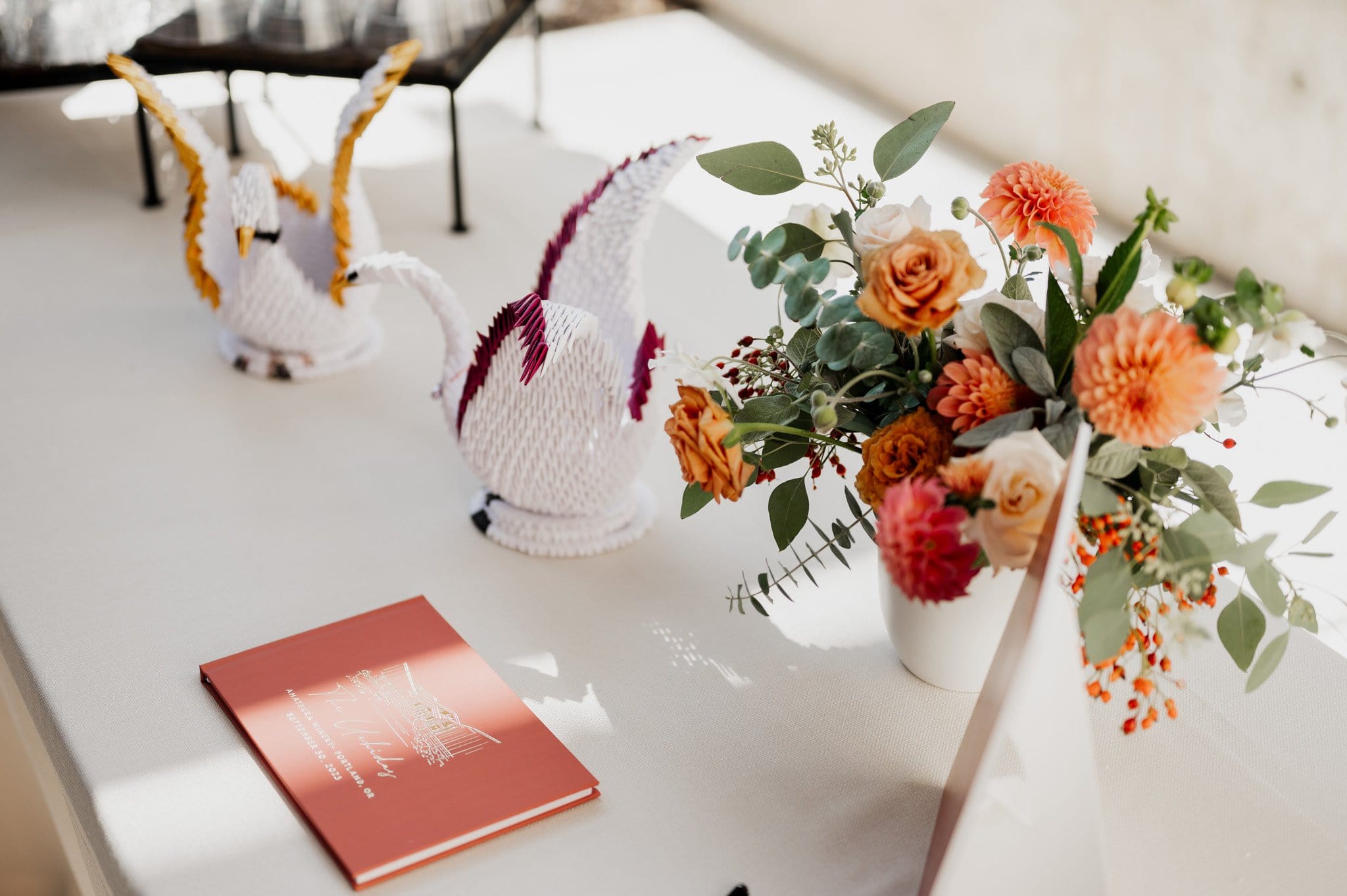 A table adorned with origami cranes, a floral arrangement, and a red book awaits the capturing of Amaterra Winery wedding photos.