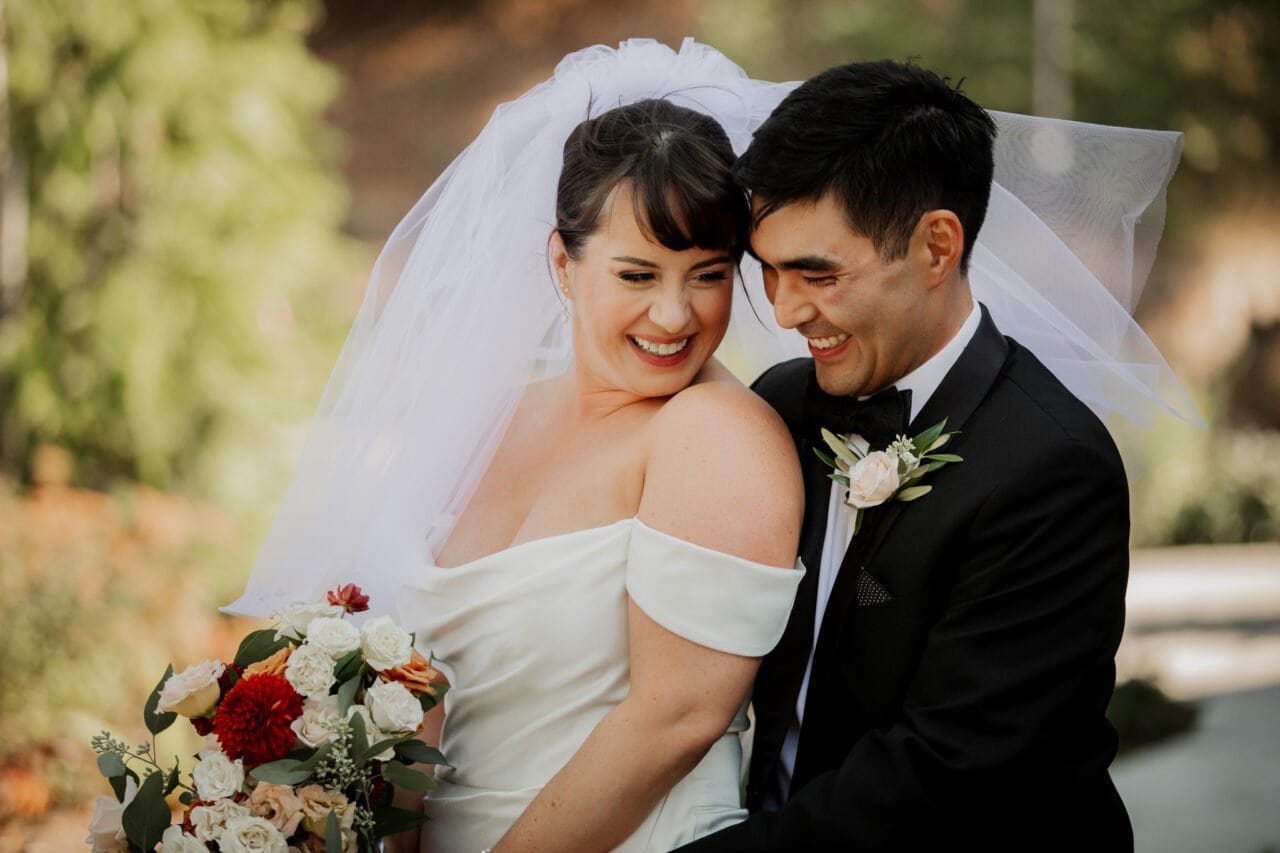 Bride and groom beaming and embracing, dressed in wedding attire at Amaterra Winery, with the bride holding a bouquet of flowers.