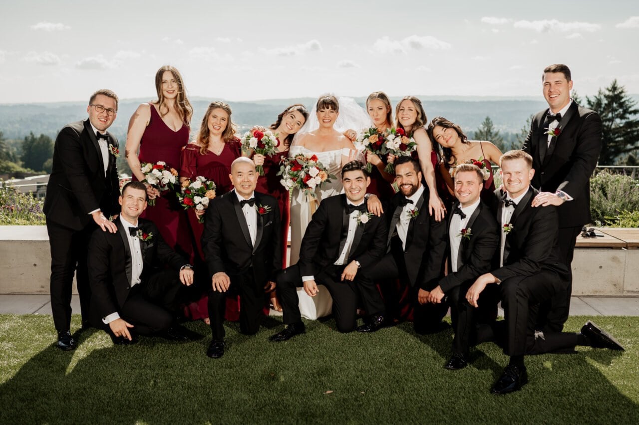 At the picturesque Amaterra Winery, the wedding party poses outdoors, with bridesmaids in red dresses and groomsmen in black suits holding elegant bouquets. Documenting this enchanting moment are the beautiful wedding photos amidst vineyard vistas.