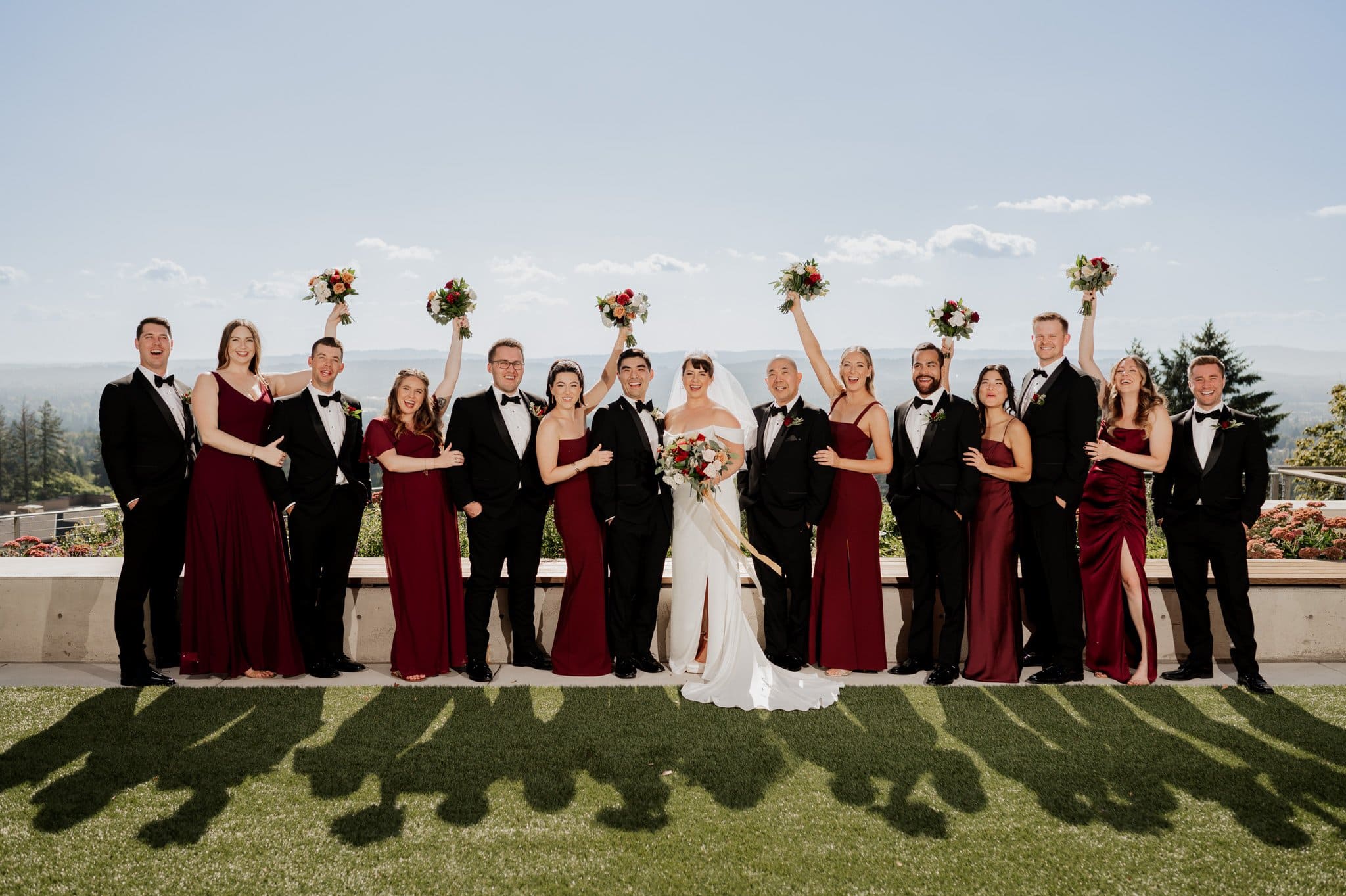 Bride, groom, and wedding party in formal attire pose outdoors at Amaterra Winery, holding bouquets and smiling against a scenic backdrop.