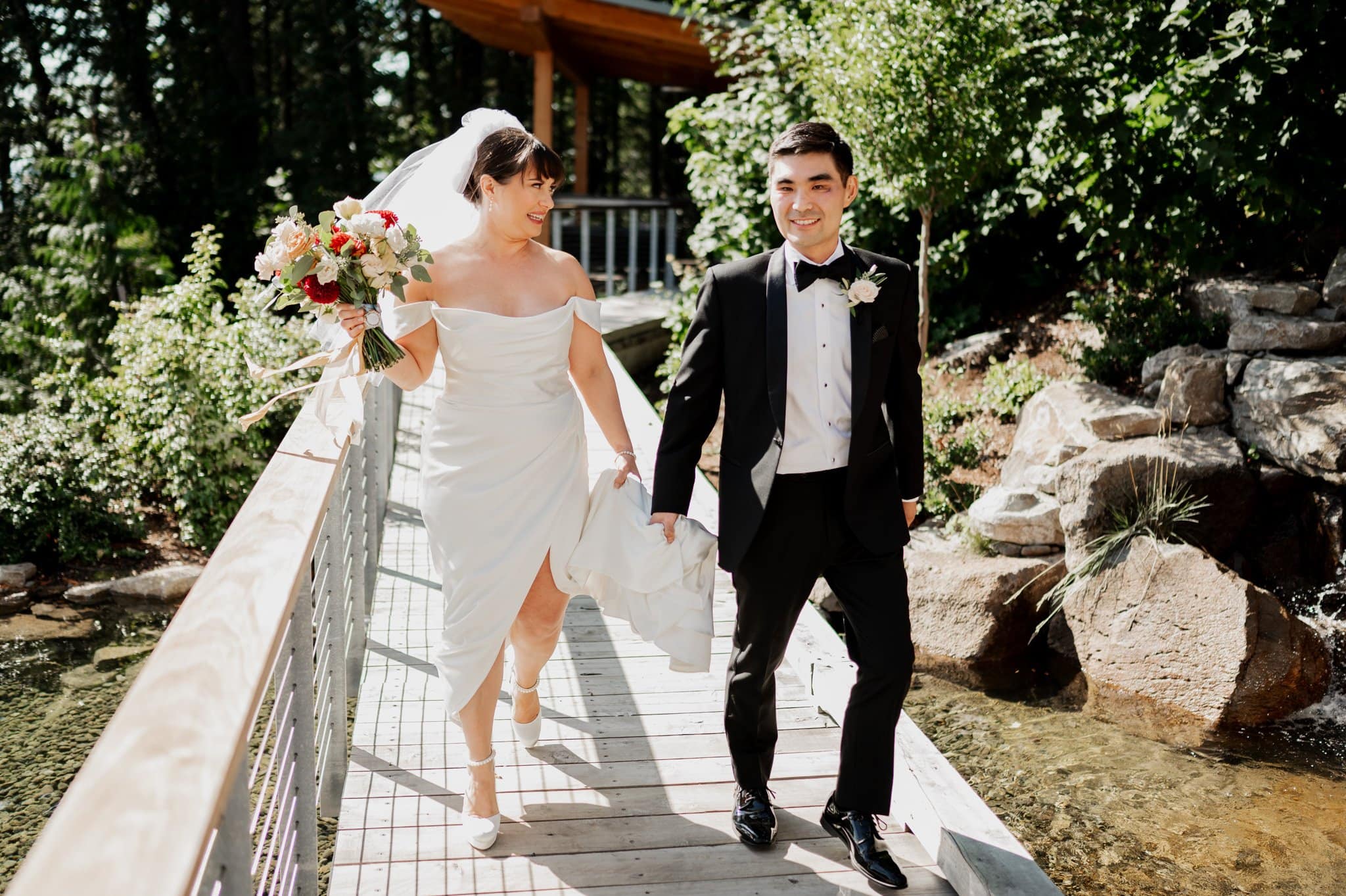 Bride and groom holding hands, walking on a bridge at Amaterra Winery, surrounded by lush greenery and sunlight.