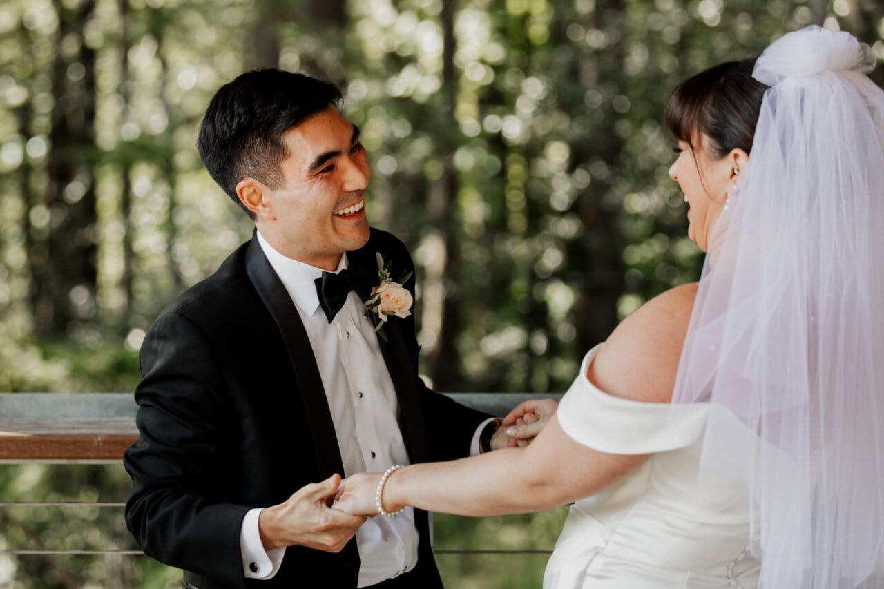 Bride and groom laughing while holding hands outdoors, surrounded by trees, with their joy perfectly captured in stunning Amaterra Winery wedding photos.
