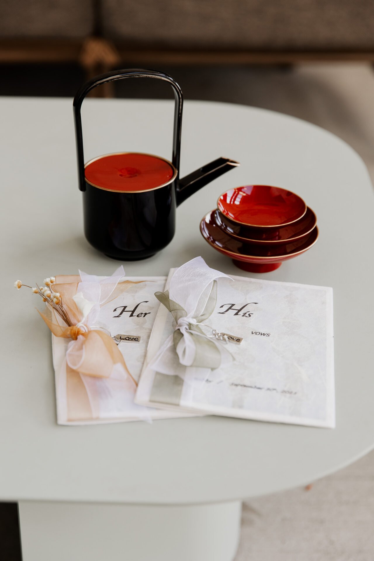 An elegant tea set with a black teapot and red cups is artfully arranged beside wedding vow books tied with ribbon on a table, capturing a moment fit for Amaterra Winery wedding photos.