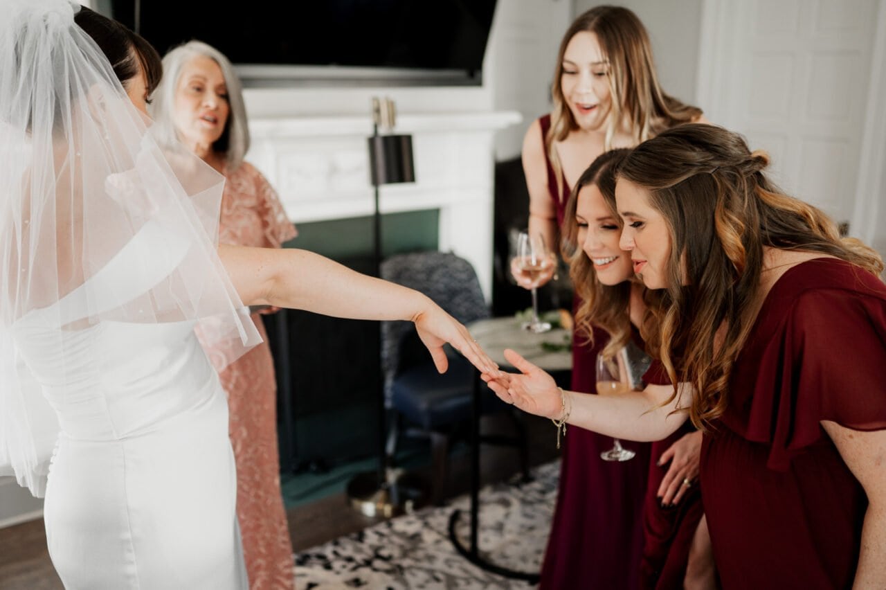 Bride shows off her ring to bridesmaids in a lively living room, all glowing with excitement as they get ready at The Heathman Hotel for an Amaterra Winery wedding.