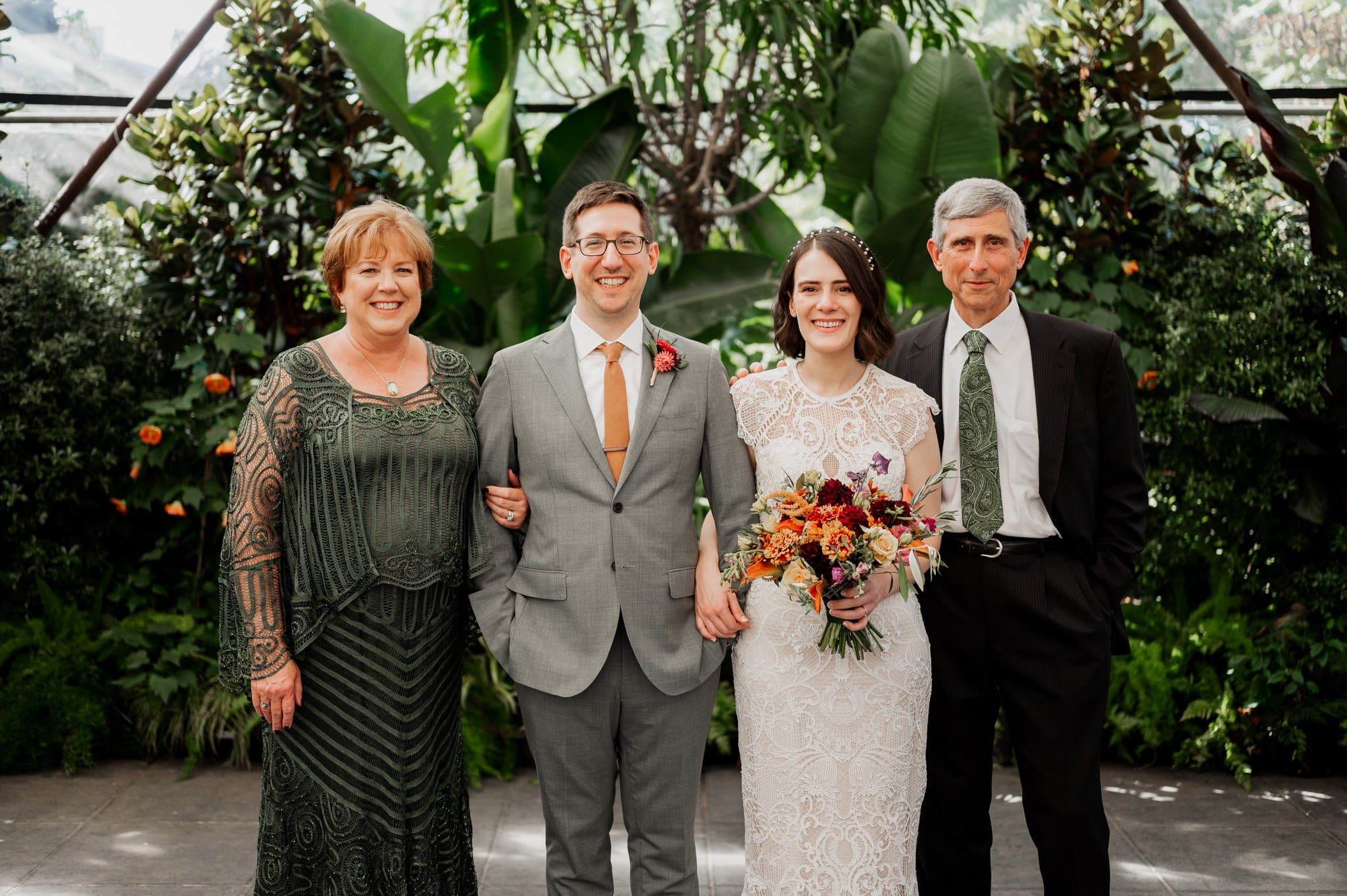 Four people, including a beaming bride and groom, pose smiling in front of lush greenery at Blockhouse, a charming Portland wedding venue.
