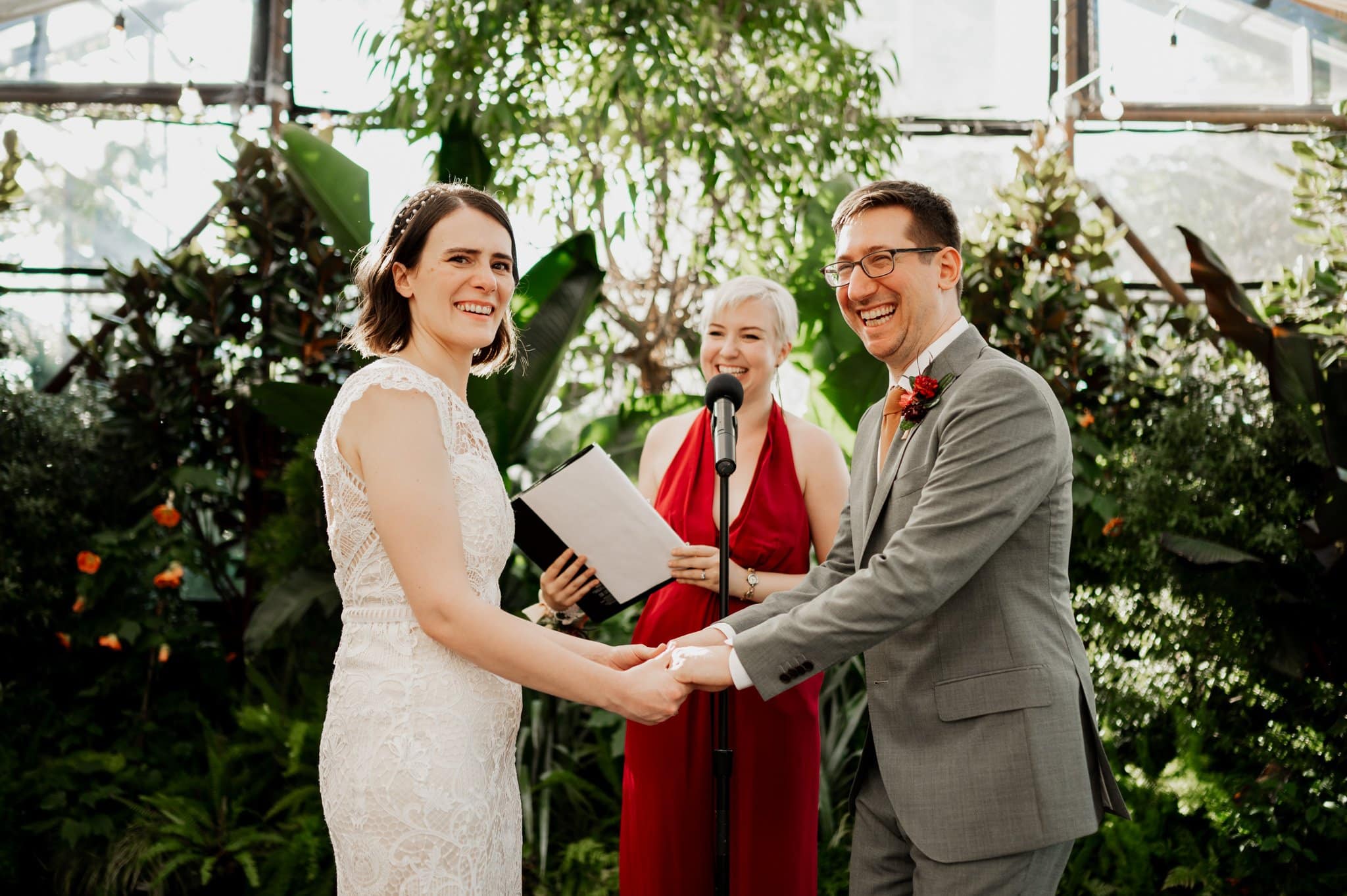 A couple holding hands and smiling during their wedding ceremony at Blockhouse, a charming Portland wedding venue, with a person officiating in the background.