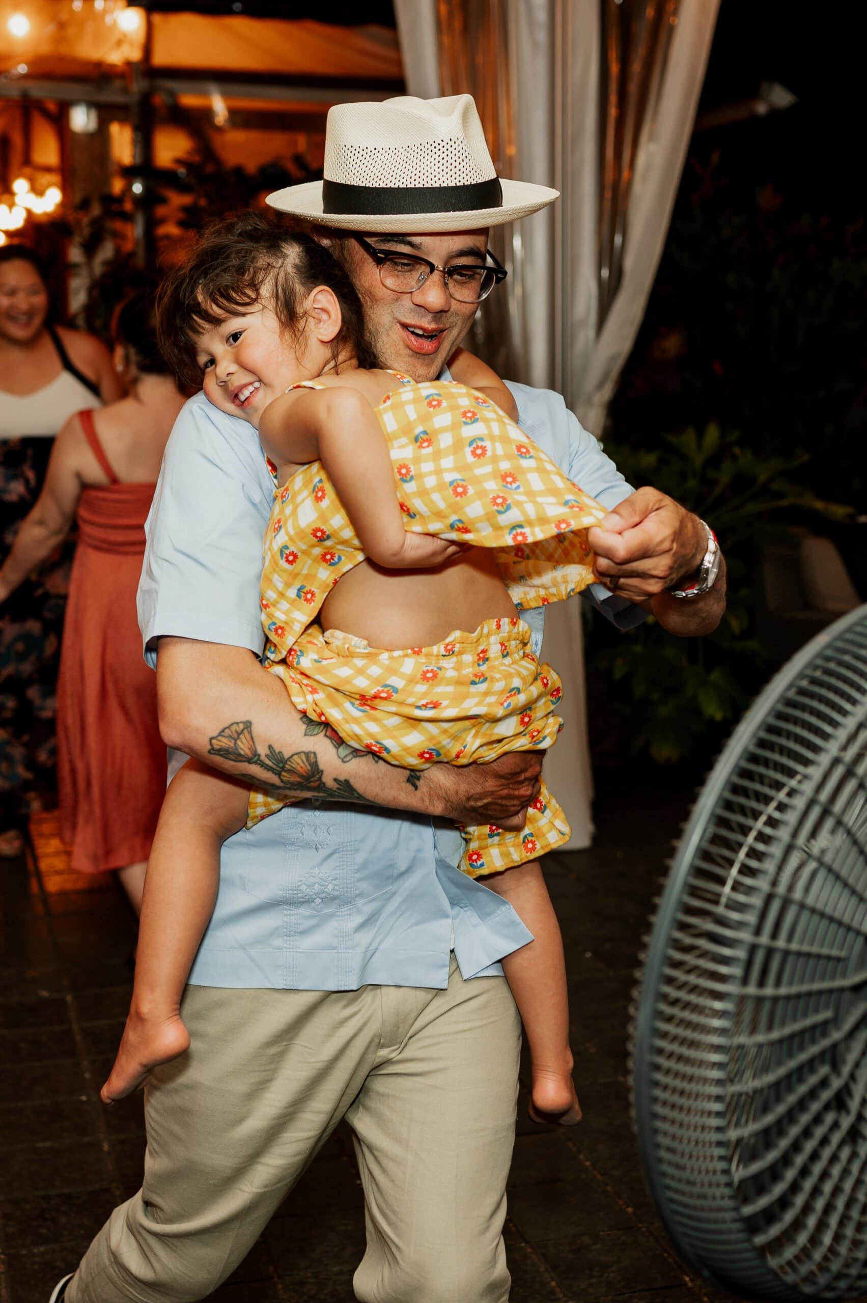 At an outdoor event, a man joyfully dances while holding a smiling girl in a yellow dress, capturing the essence of wedding photos at Blockhouse.