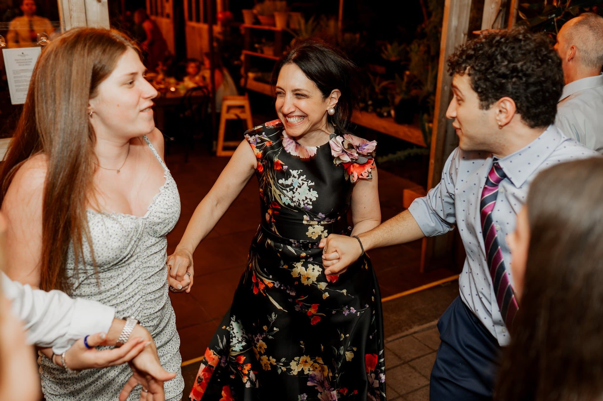 Three people are joyfully holding hands and smiling while dancing at a lively indoor event, perfect for capturing wedding photos at Blockhouse.