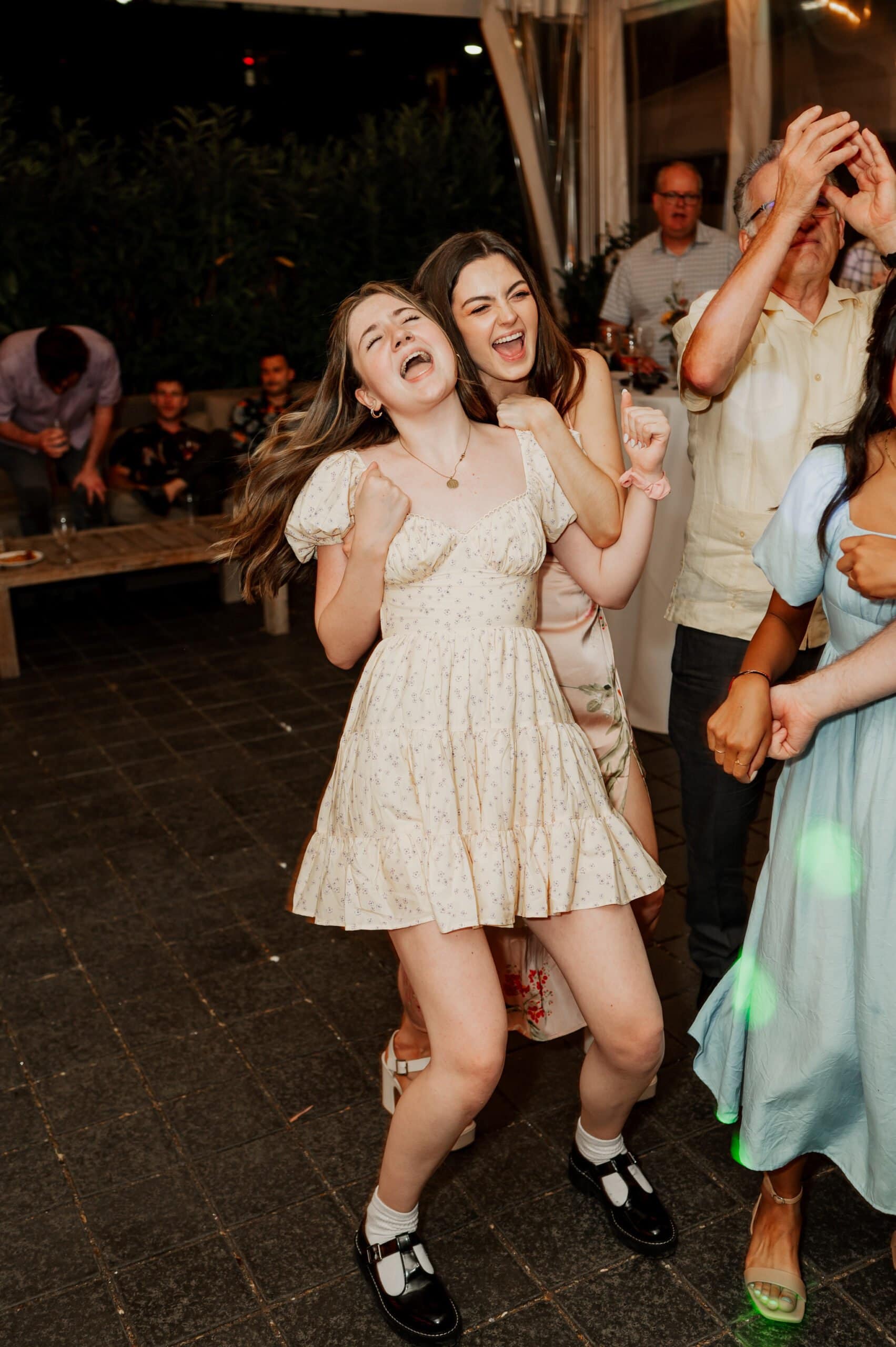 Two women joyfully dancing with others at a lively indoor wedding event, captured beautifully in photos at Blockhouse.