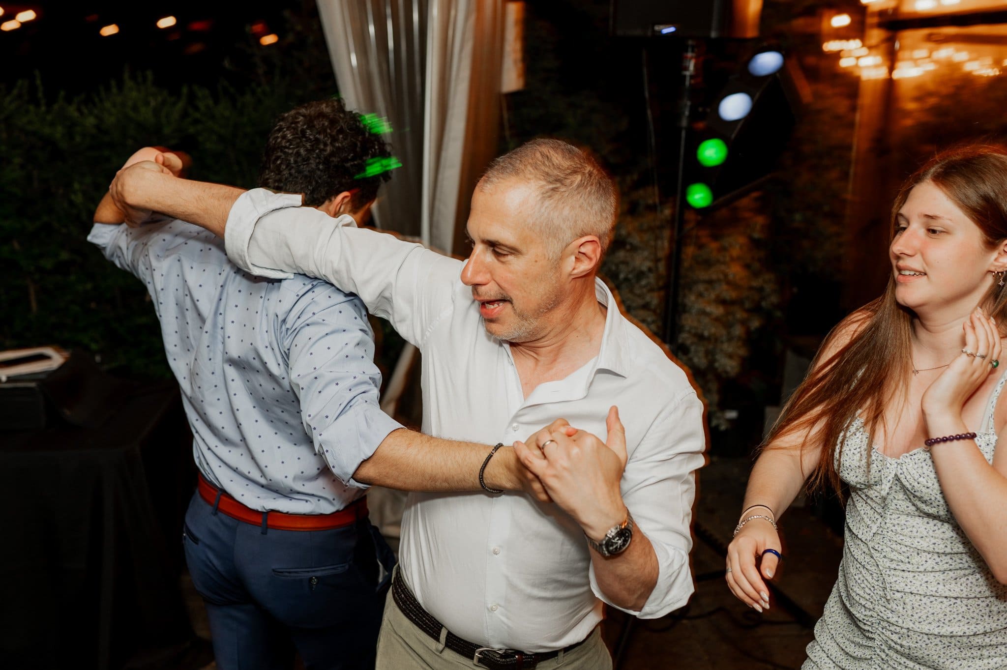 Three people dance lively at a party amid vibrant lights, capturing a moment reminiscent of wedding photos at Blockhouse.