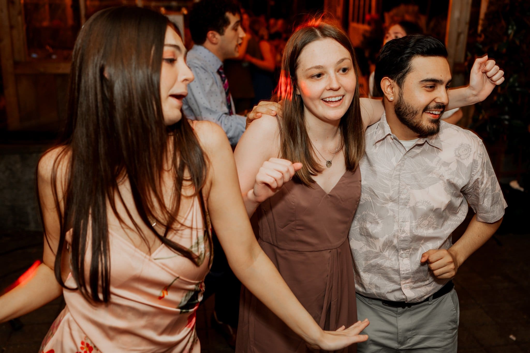 Three people dancing together at a lively party, smiling and enjoying the moment under warm lighting, capturing the joy found in wedding photos at Blockhouse.