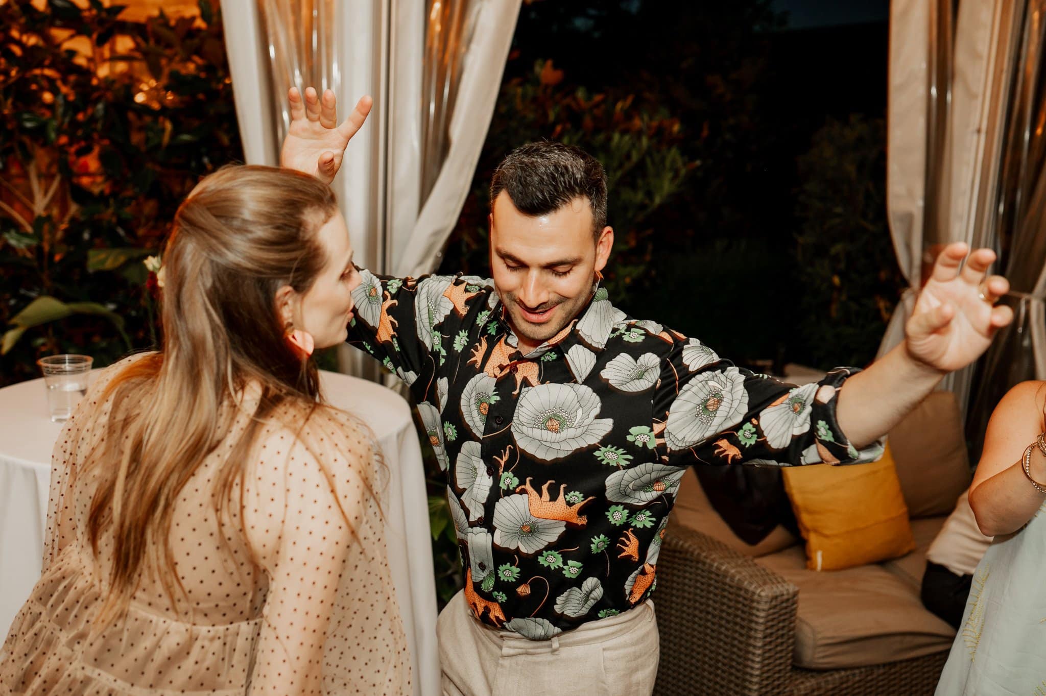 A man in a floral shirt dances with a woman in a beige dress at an outdoor wedding event, capturing joyful moments perfect for wedding photos at Blockhouse.