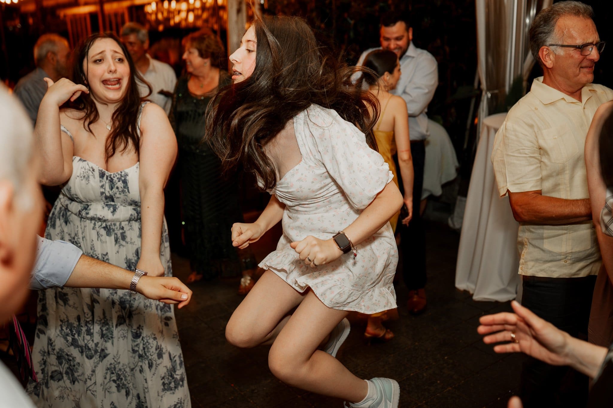 At the lively event, guests dance energetically under colorful lights and decorations. The joyful atmosphere is captured beautifully, much like wedding photos at Blockhouse.