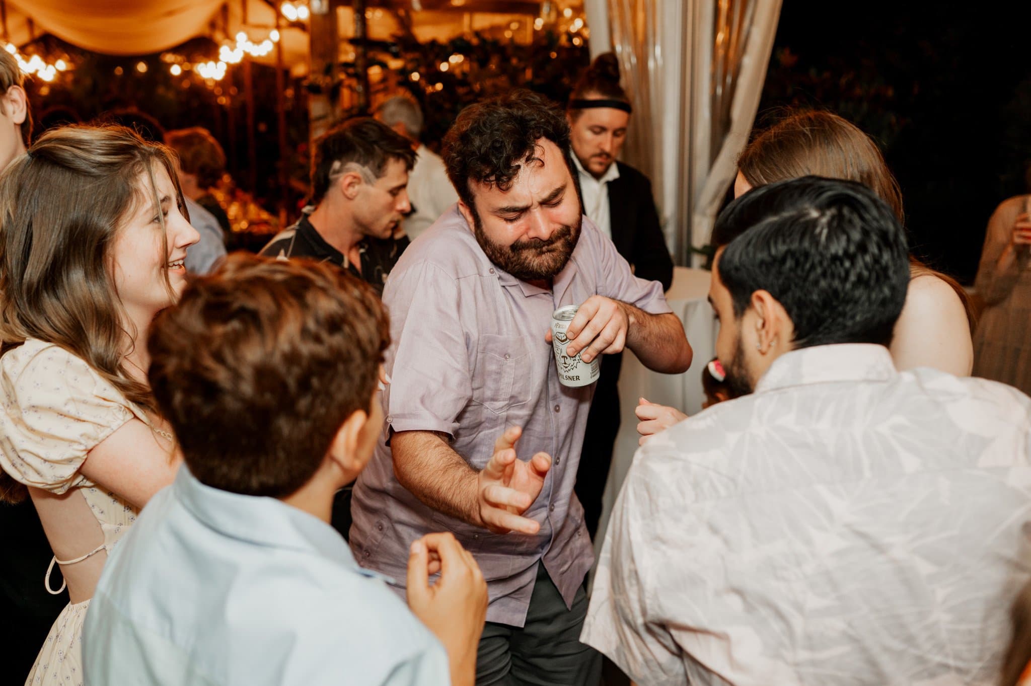 Guests are dancing energetically at a lively indoor party, with one man holding a can and others smiling and engaging. Its reminiscent of wedding photos at Blockhouse, capturing the joy of everyone celebrating together.