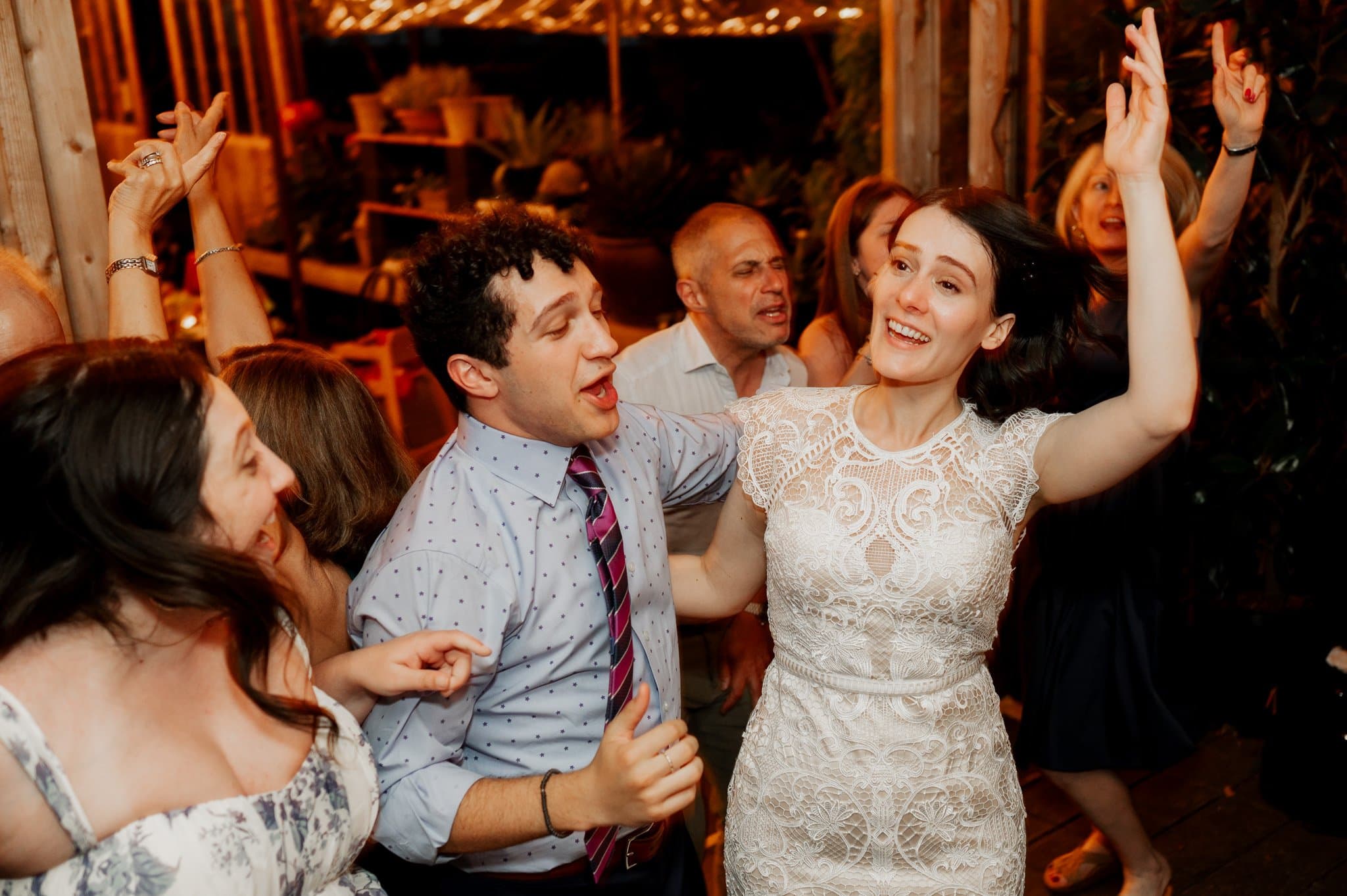 People dancing and celebrating at an outdoor party with warm lighting and cheerful expressions, capturing the joy of wedding photos at Blockhouse.