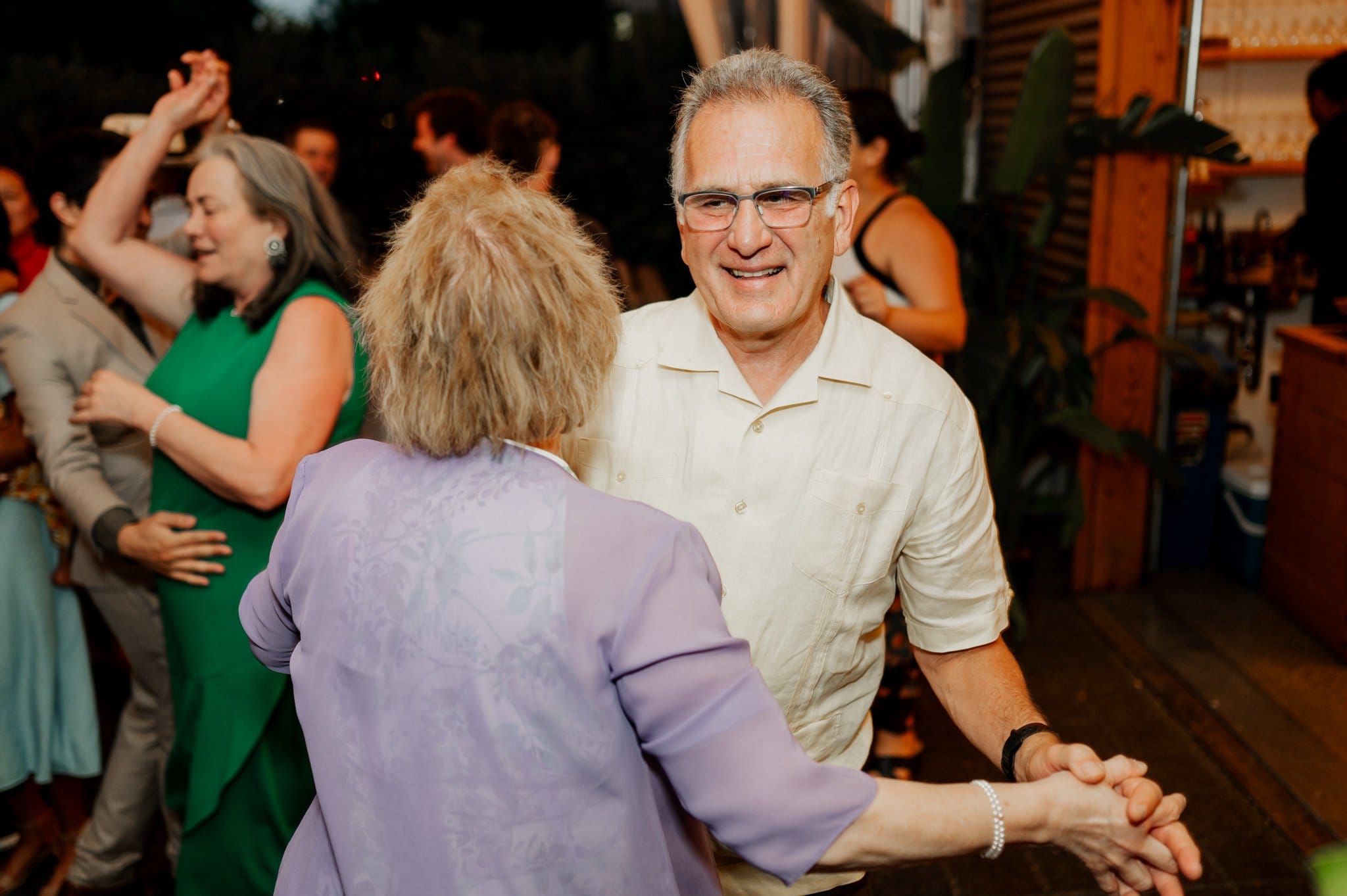 A man and woman dance joyfully at a lively indoor event, with others joining in the celebration in the background. Its a moment that could easily be captured as wedding photos at Blockhouse, encapsulating the spirit and energy of such a memorable occasion.