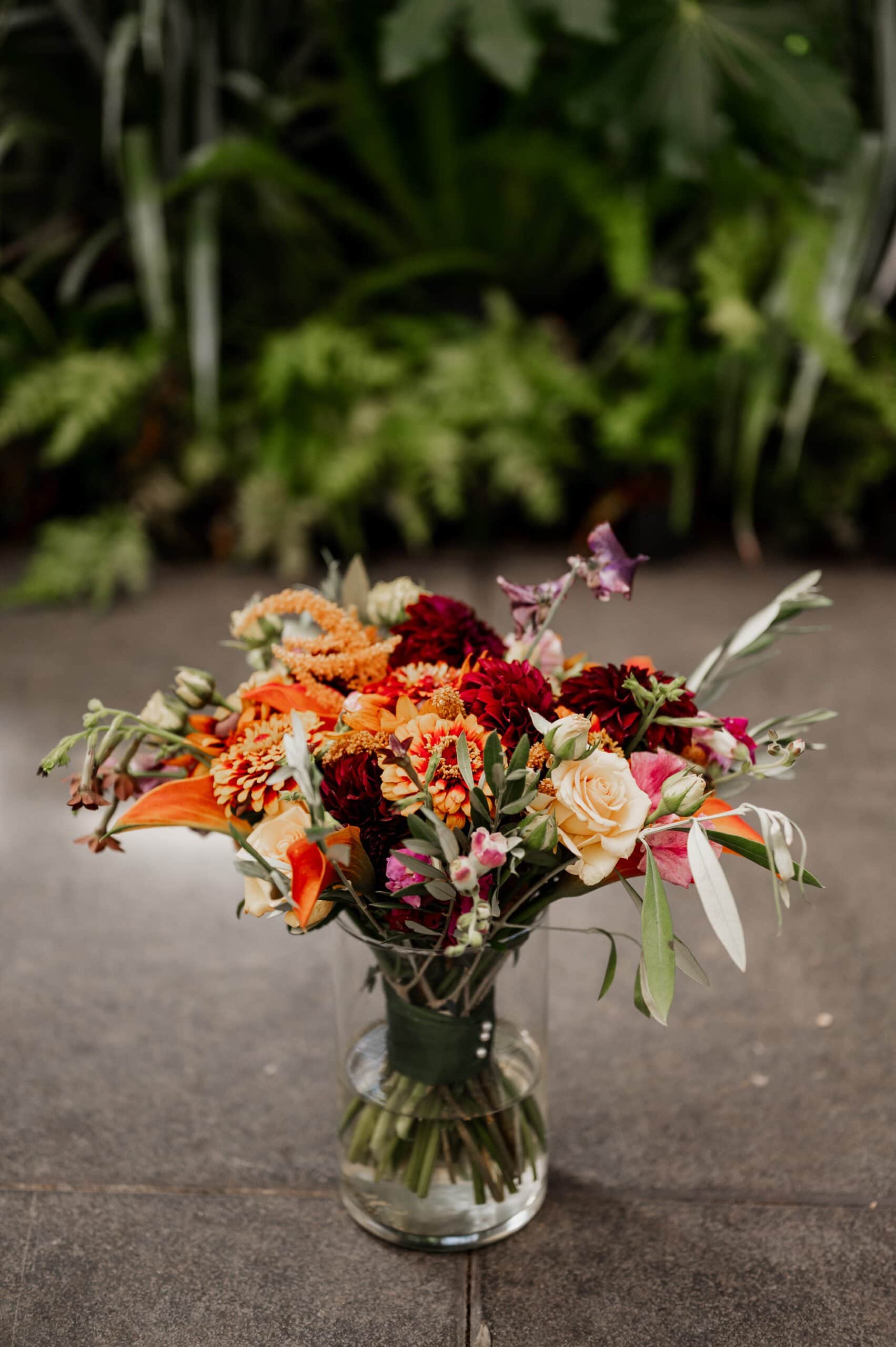 A colorful bouquet of flowers in a glass vase sits on a stone surface, with lush green foliage in the background, perfect for elegant wedding photos at Blockhouse.