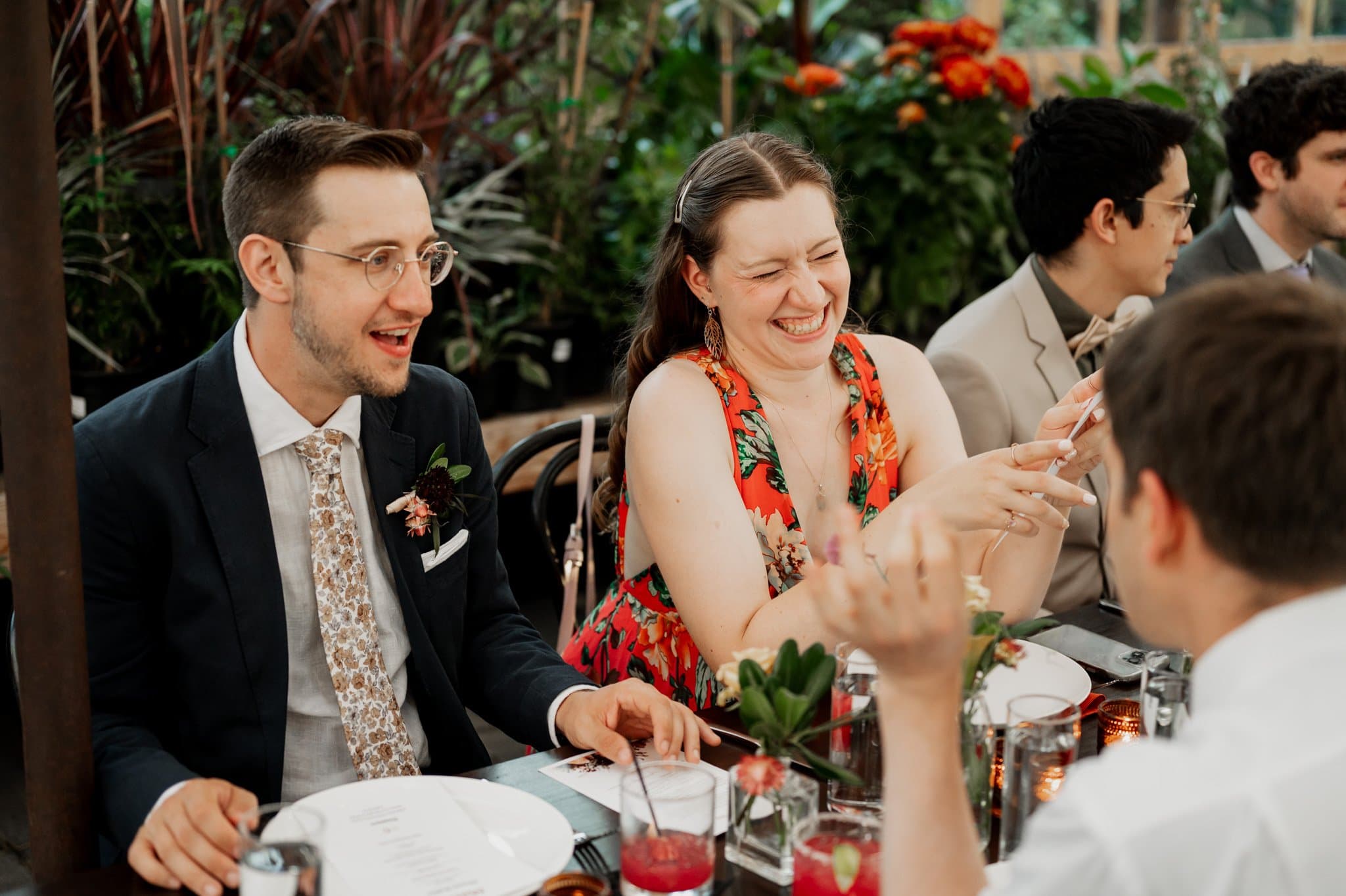 People laughing and chatting at a table, surrounded by lush plants and flowers, capturing the joyful essence of wedding photos at Blockhouse.