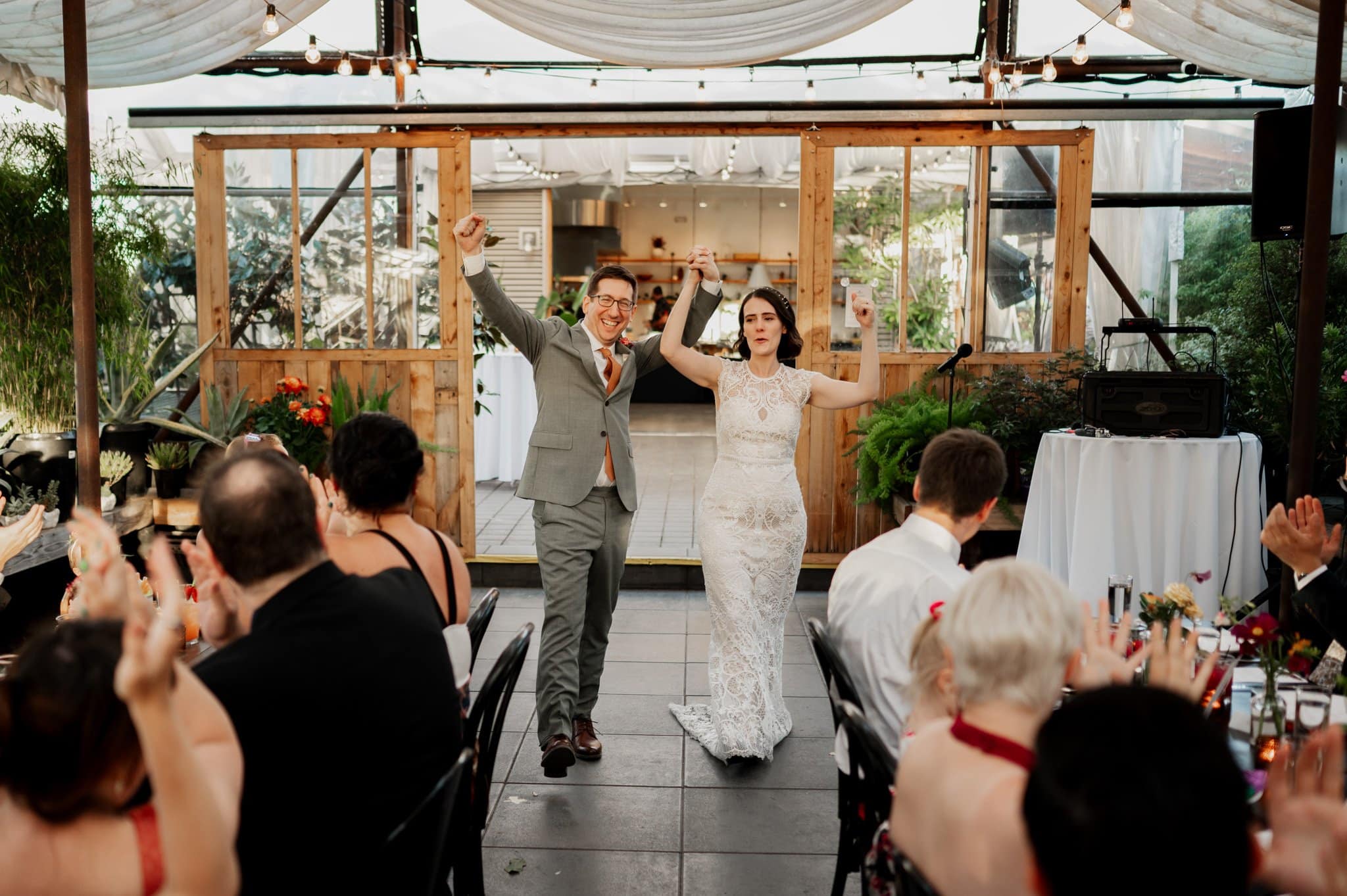 The bride and groom joyfully enter the reception at Blockhouse, welcomed by the claps and cheers of their guests amidst beautifully decorated surroundings.