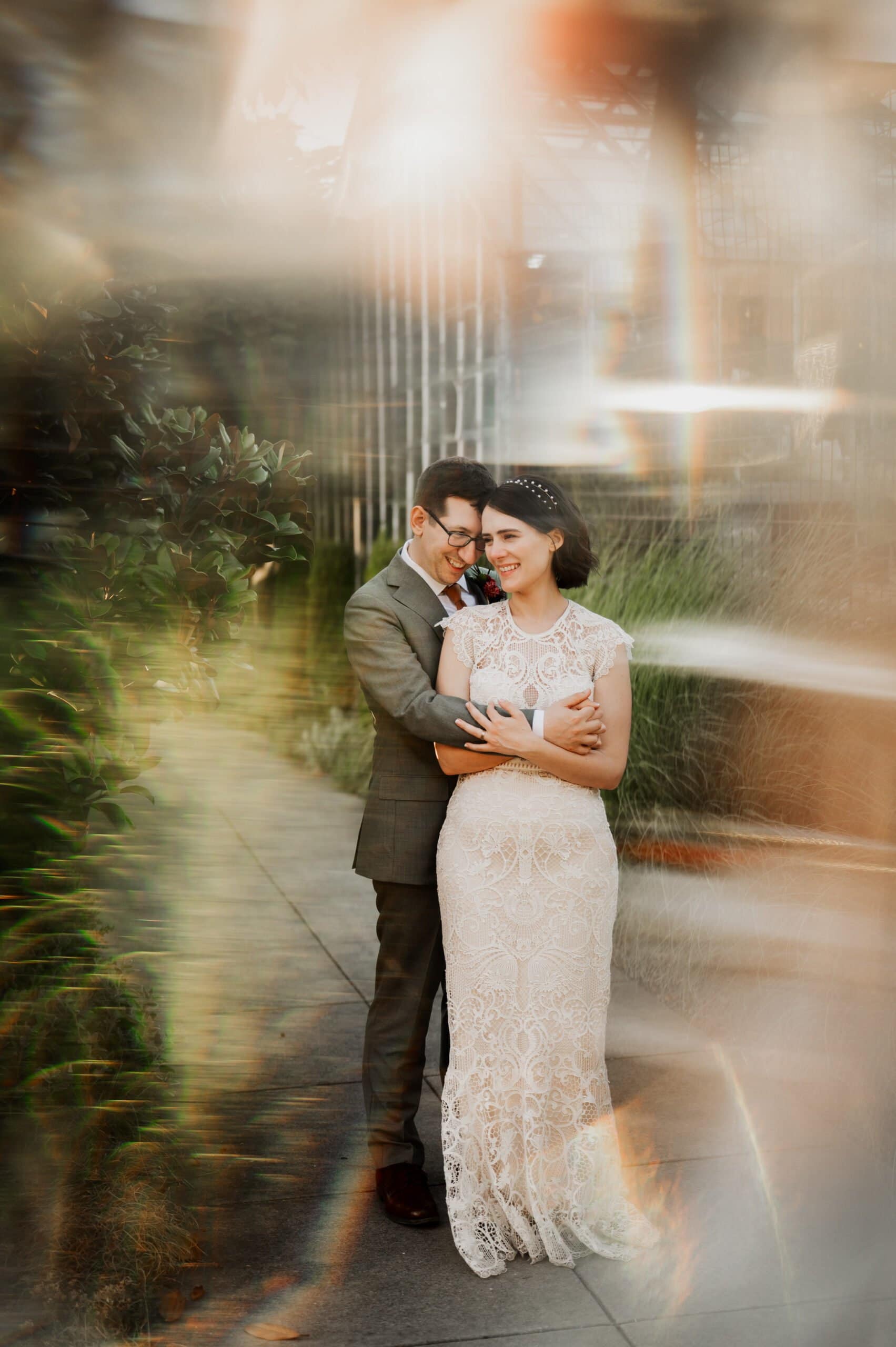 A couple embraces on a sidewalk surrounded by colorful light effects. The woman is dressed in a lace dress, capturing a moment reminiscent of wedding photos at Blockhouse.