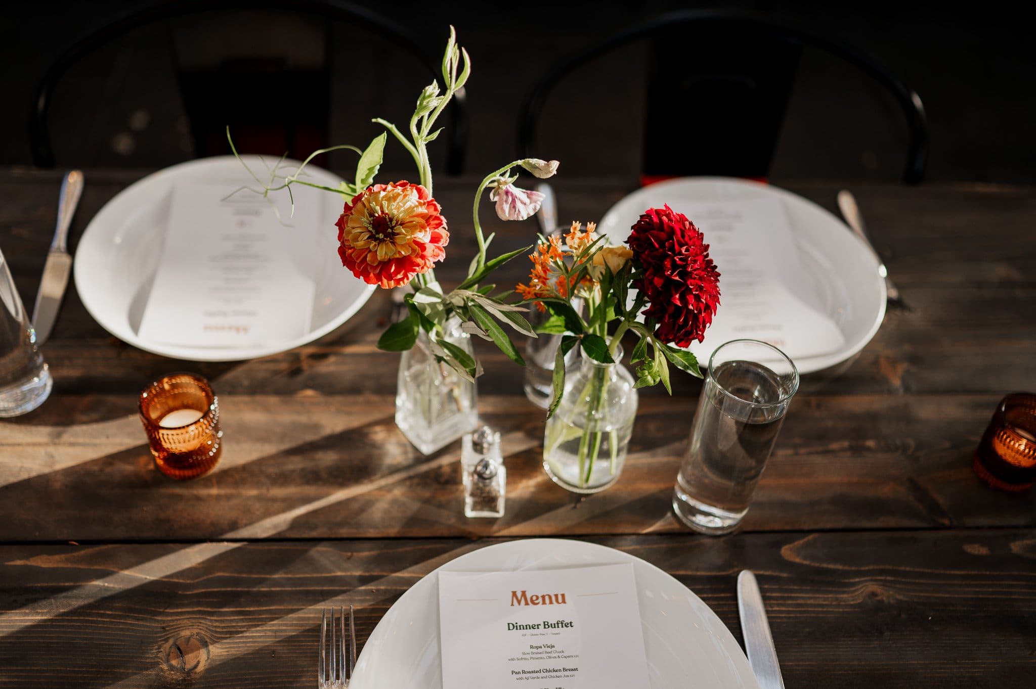 A wooden table set for a meal with floral centerpieces, menus, and orange candles, ready for wedding photos at Blockhouse.