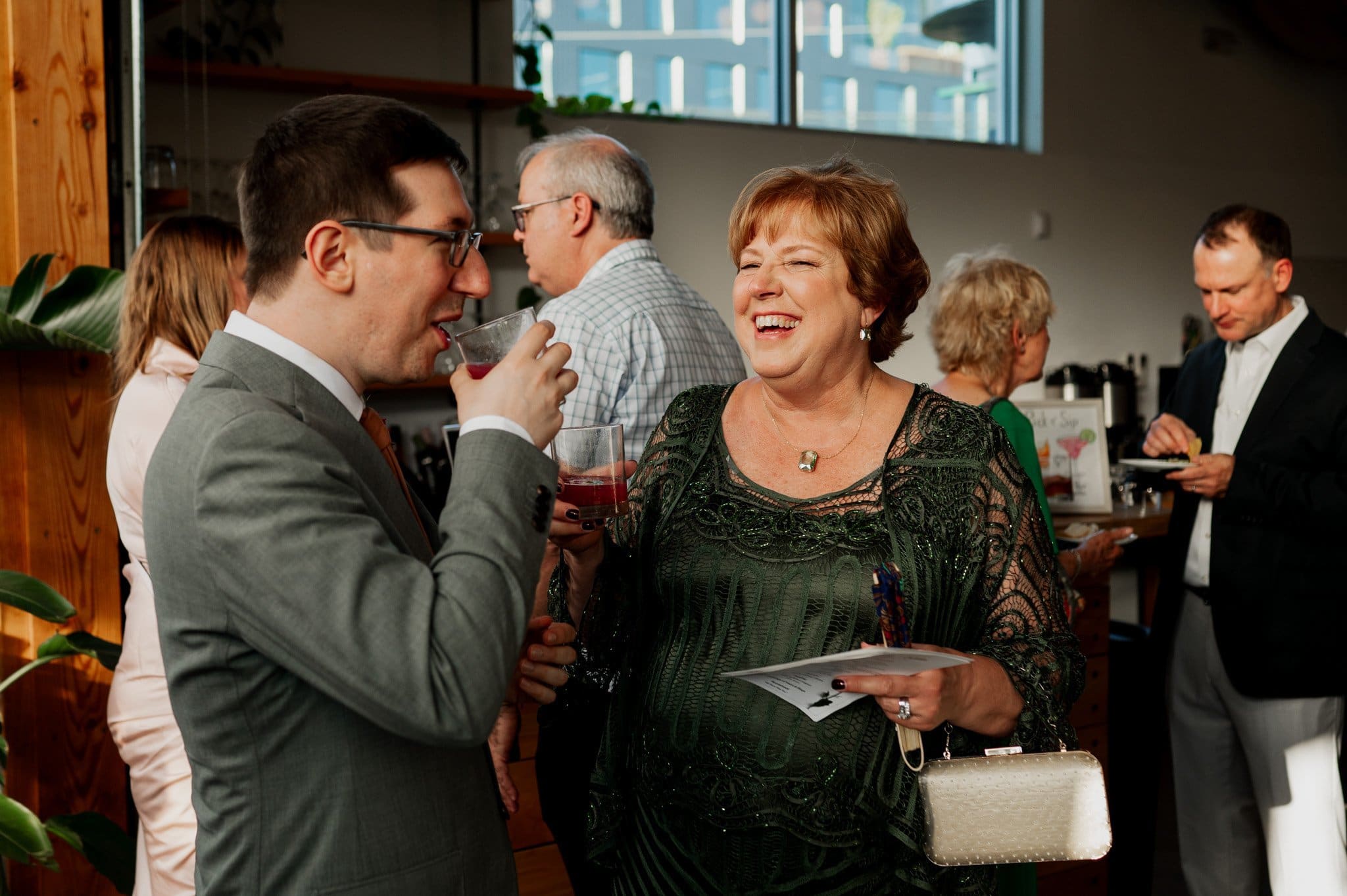 Two people smiling and chatting at a social gathering, with others mingling in the background, reminiscent of joyous wedding photos at Blockhouse.