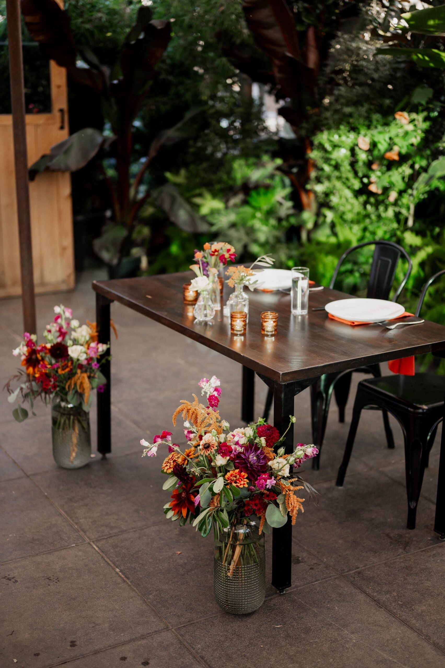 An outdoor table with vibrant floral arrangements is set for dining amidst lush greenery, offering the perfect backdrop for wedding photos at Blockhouse.