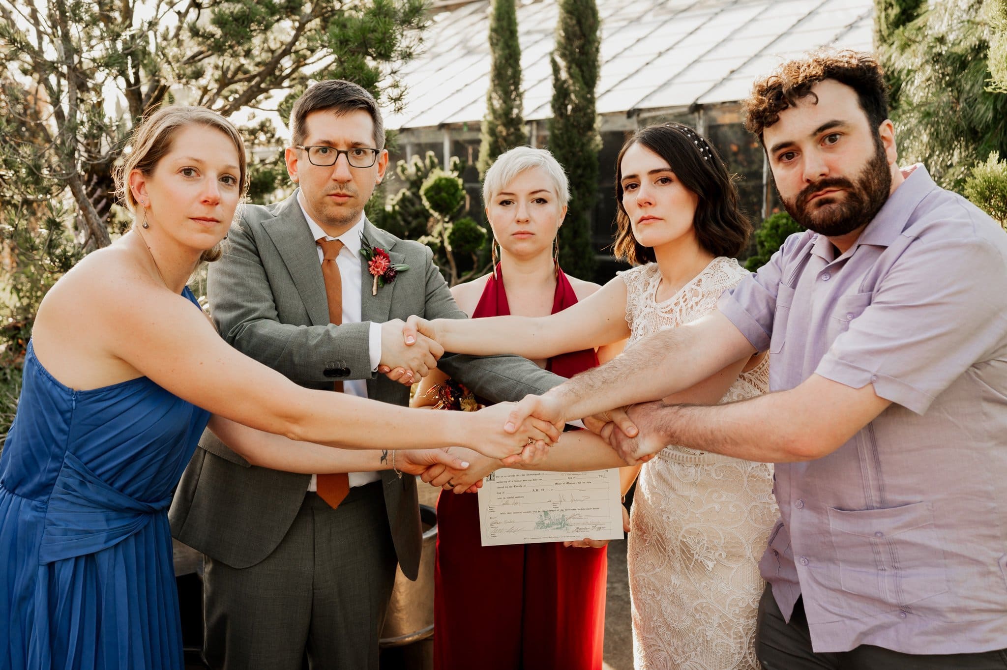 Five people in formal attire gather at Blockhouse, holding a document together, standing outdoors amidst the trees.