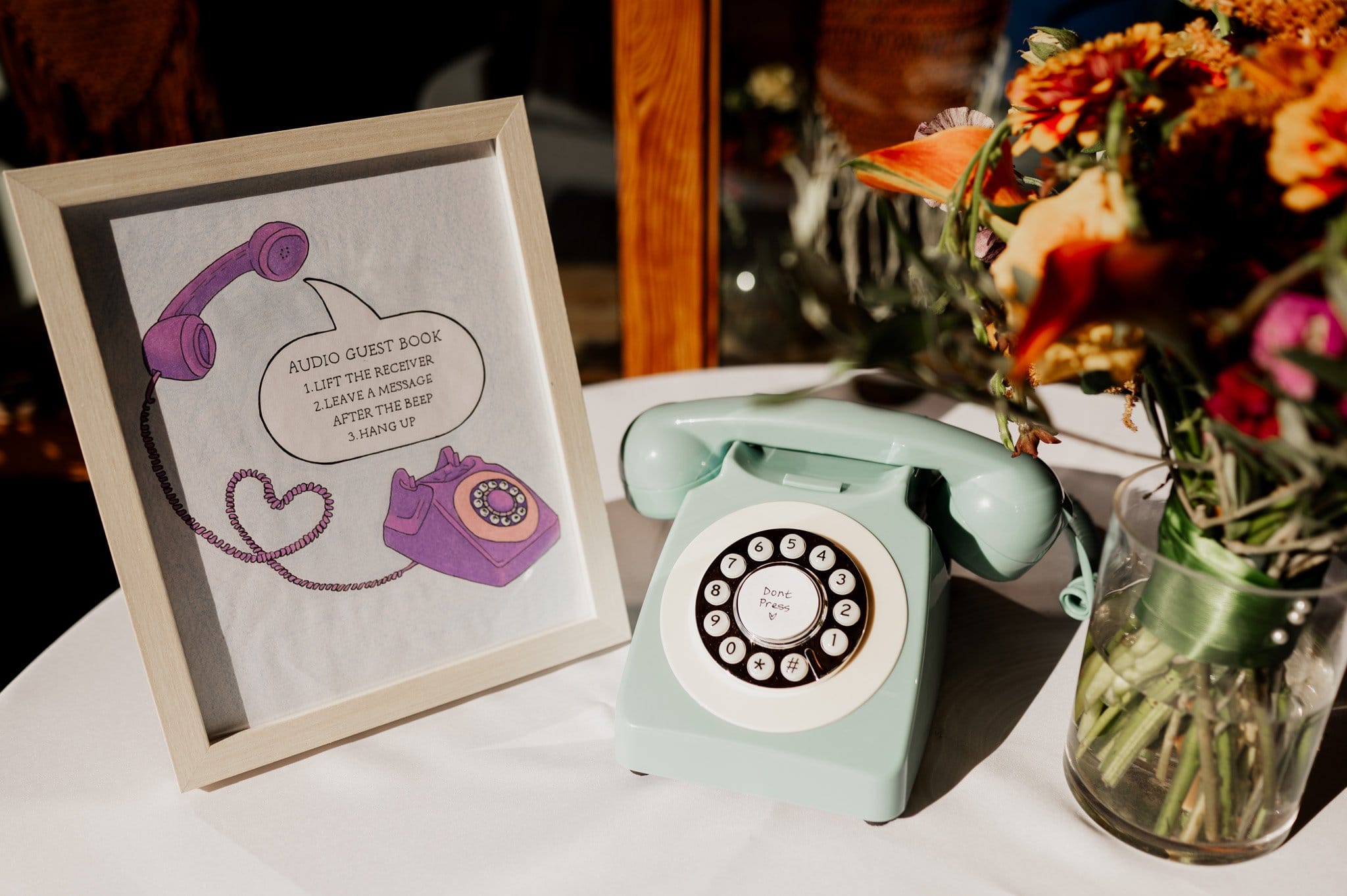 A vintage mint rotary phone stands beside a framed sign for an audio guest book, surrounded by flowers. Perfect for wedding photos at Blockhouse, this charming setup adds a touch of nostalgia to any event.