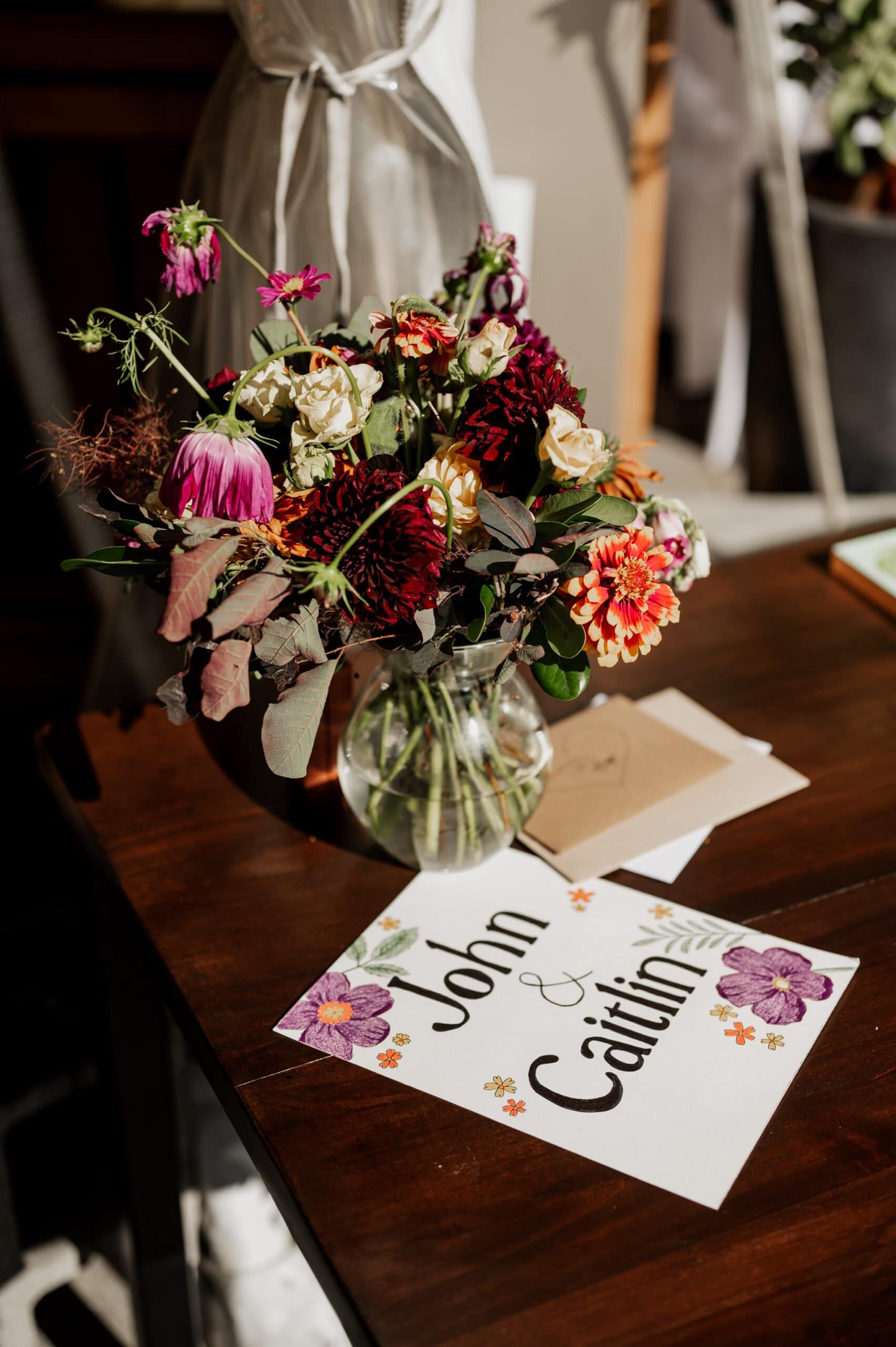 A bouquet of vibrant flowers in a vase sits on a wooden table next to a card reading John & Caitlin, capturing the elegance of wedding photos at Blockhouse.