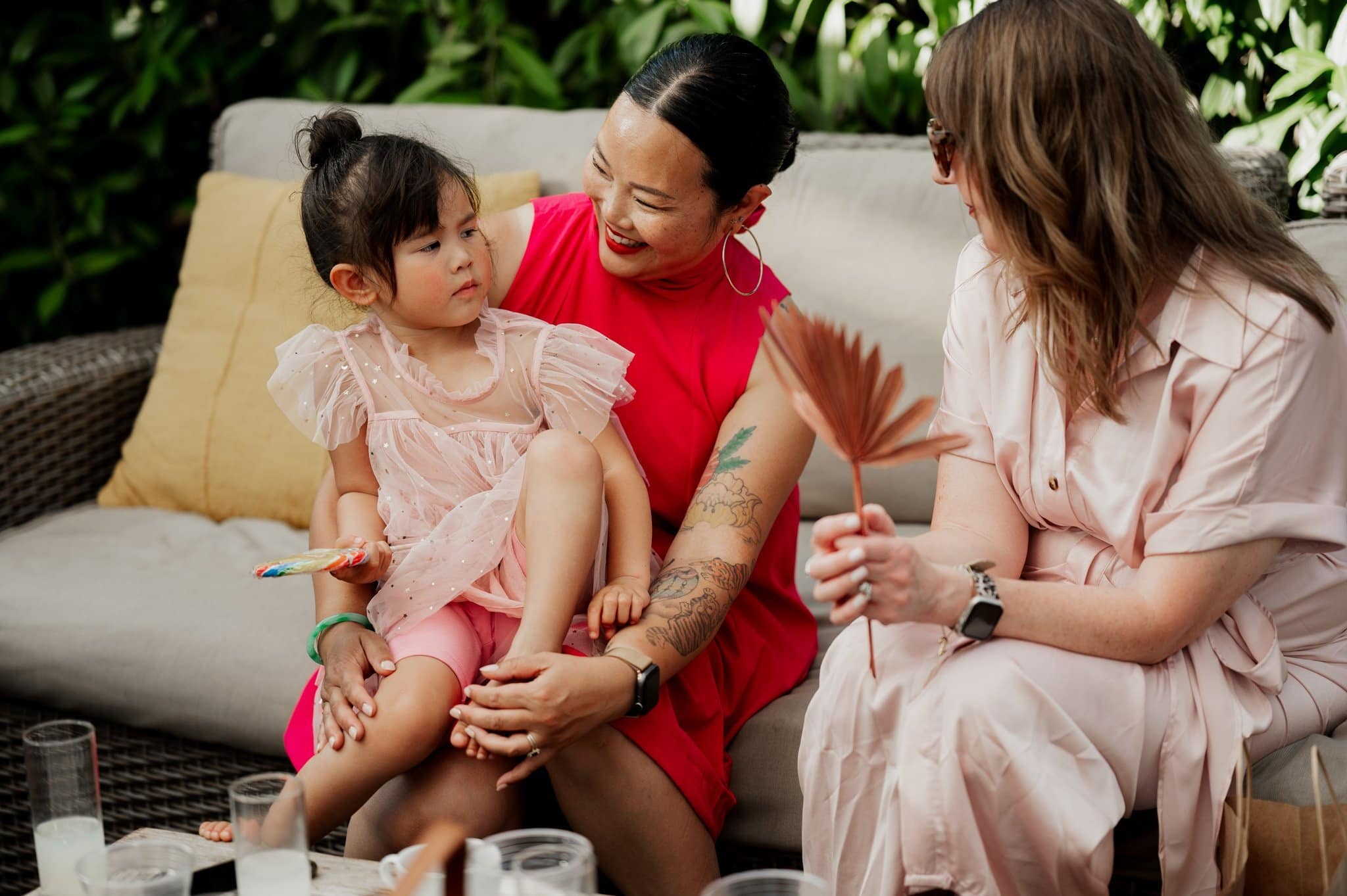 Three people sitting outdoors on a sofa, two adults and a child, engaged in conversation and smiling warmly, as if sharing cherished memories from wedding photos taken at Blockhouse.