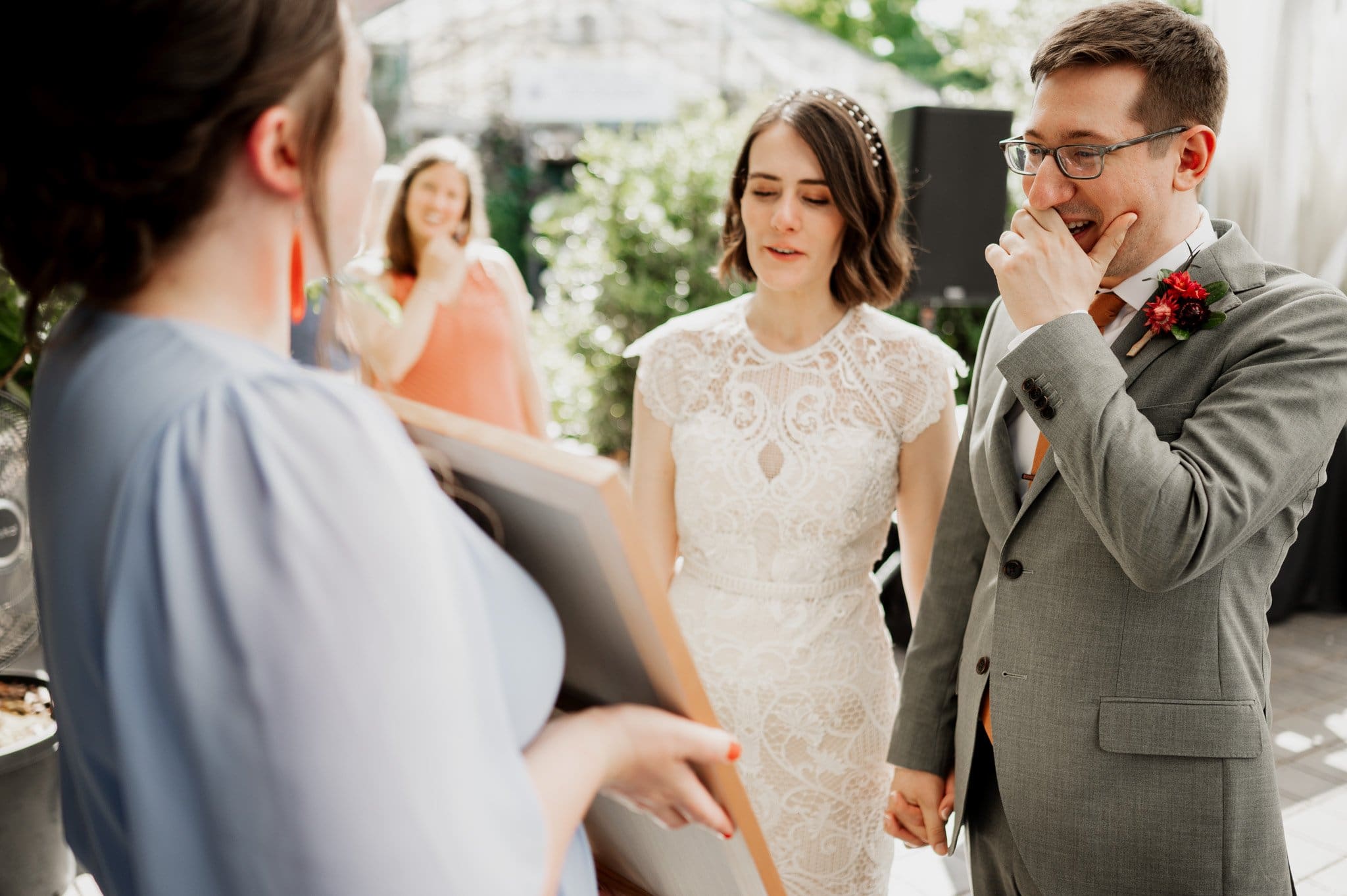 The bride and groom react joyfully during an outdoor ceremony, captured perfectly in wedding photos at Blockhouse. Another woman holds a document in front of them.