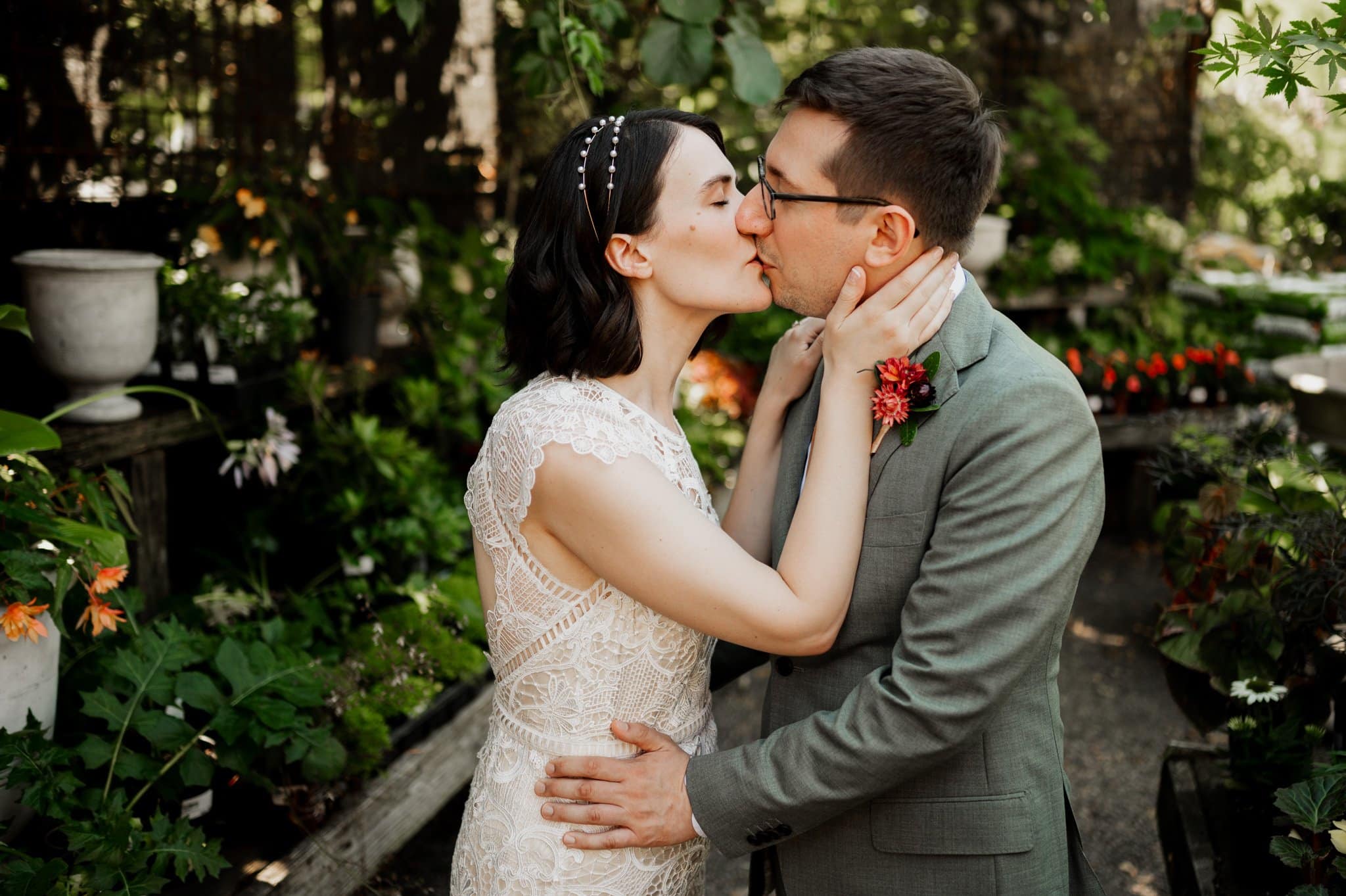 In a lush garden setting, a couple shares a tender kiss, the woman in a lace dress and the man in a suit adorned with a boutonniere. This enchanting moment captures the essence of wedding photos at Blockhouse.
