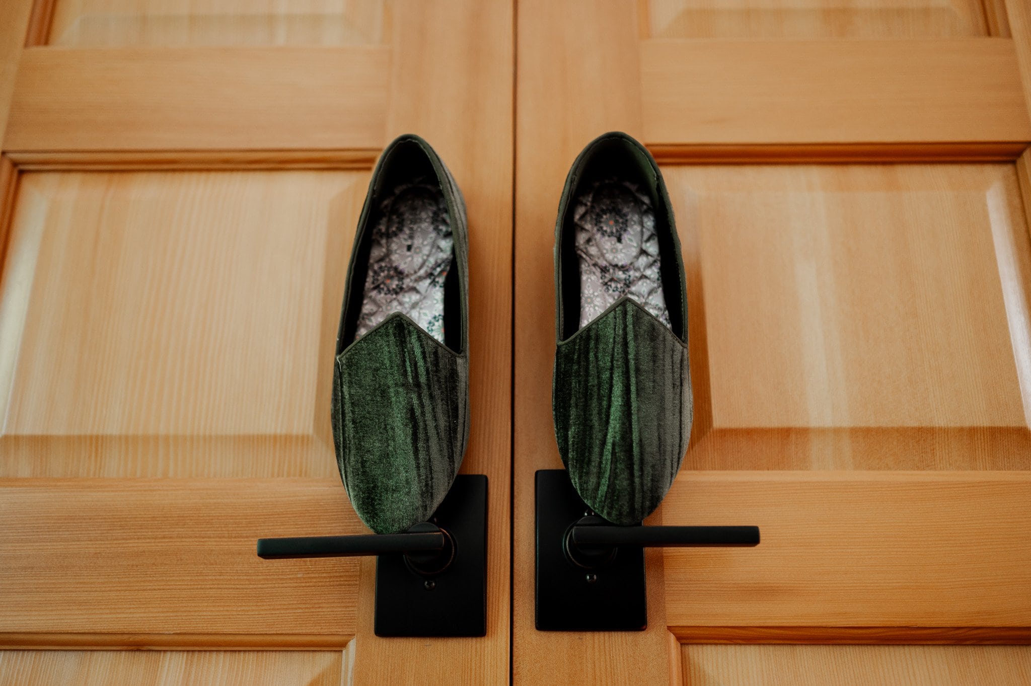 Green velvet shoes are elegantly hanging on wooden door handles, setting the stage for getting ready at an Airbnb for a wedding at Blockhouse.