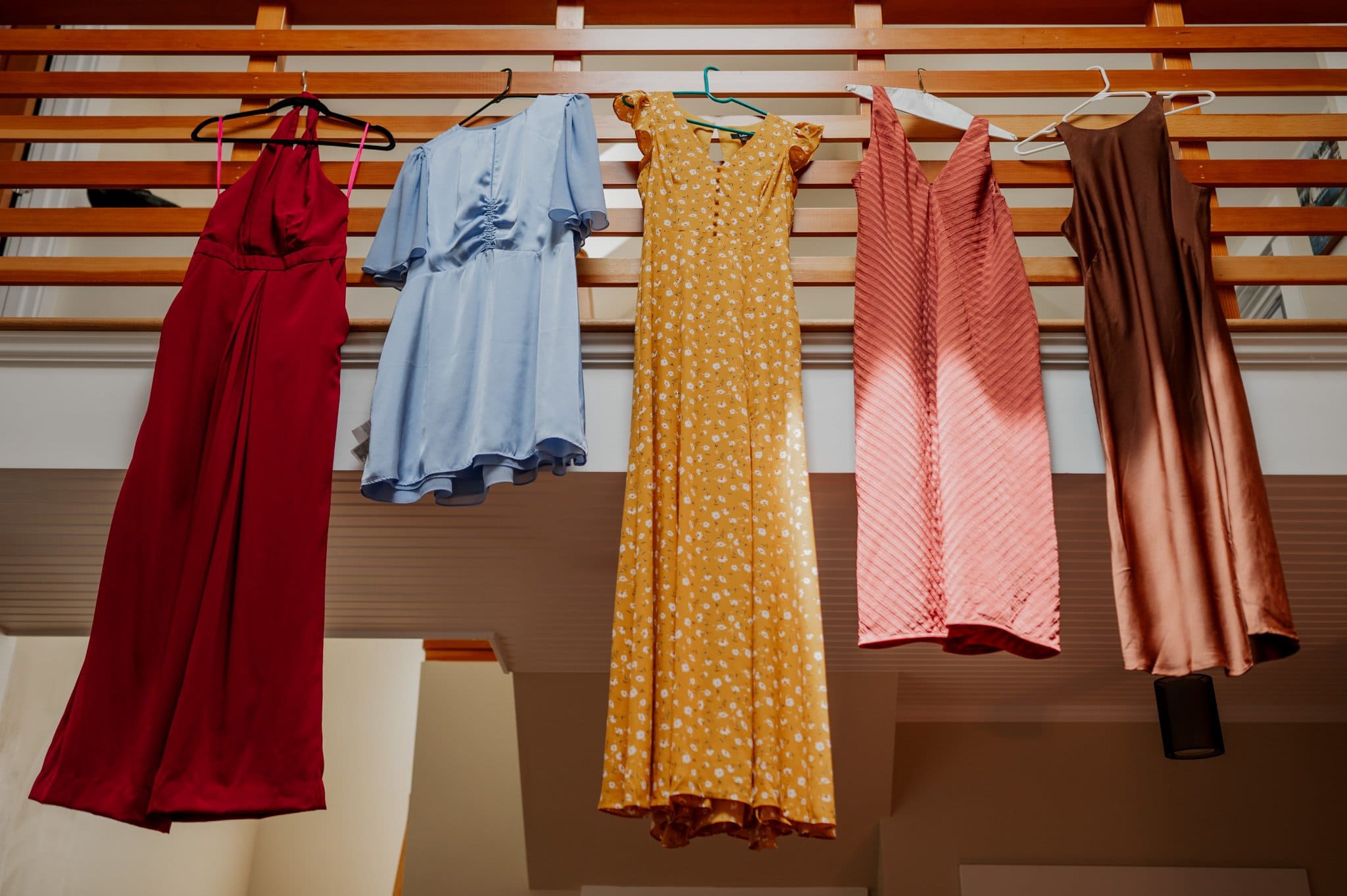 Five colorful dresses hanging on a railing indoors, ready for those getting ready at an Airbnb for a wedding at Blockhouse.