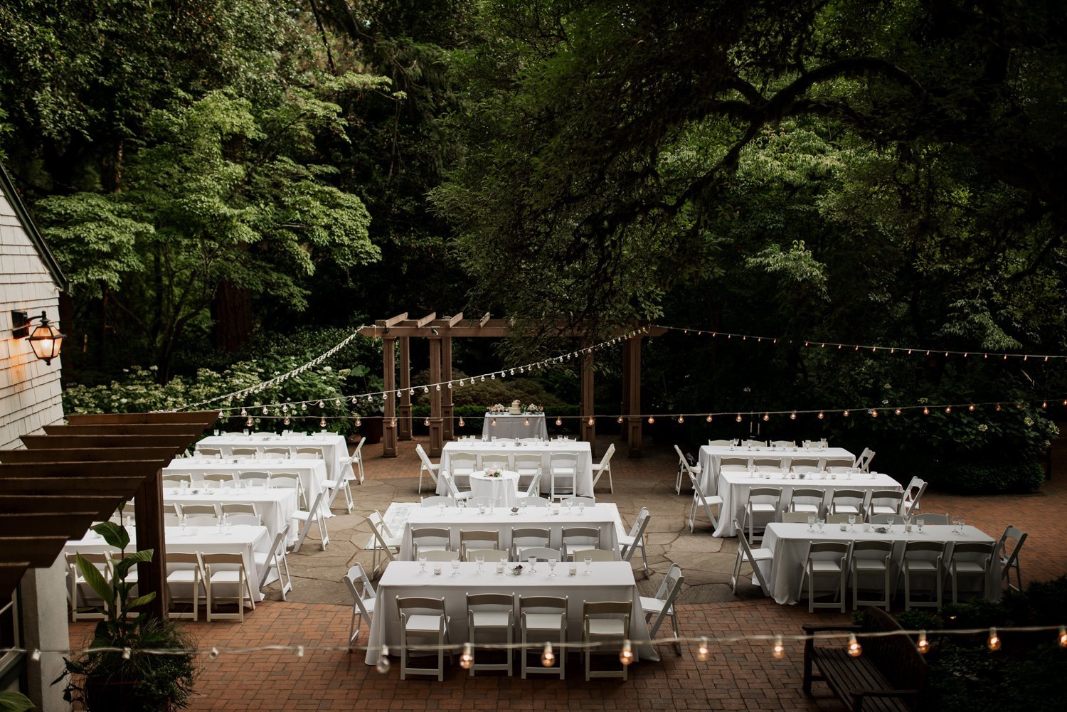 An outdoor wedding at Leach Botanical Garden with tables covered in white tablecloths, chairs arranged neatly, and string lights hanging from tree branches.